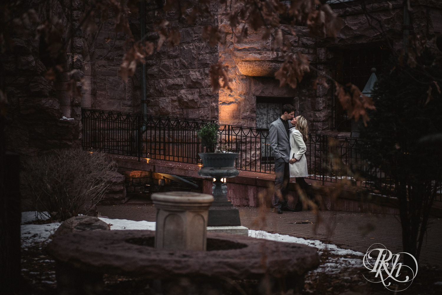Man and woman in winter coats kiss in front of the Van Dusen Mansion in Minneapolis, Minnesota.