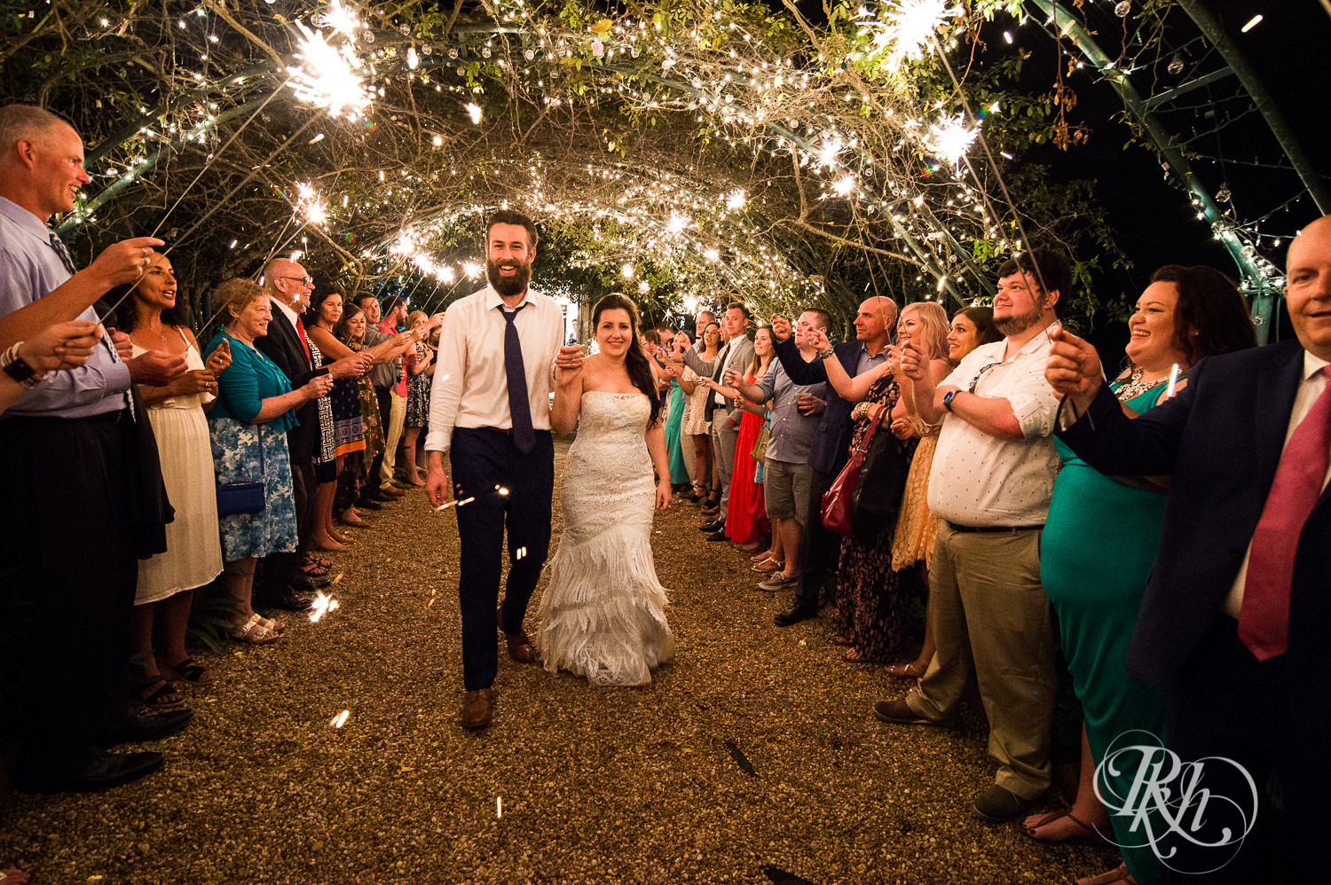 Bride and groom walk through a garden during sparkler exit with guests. 