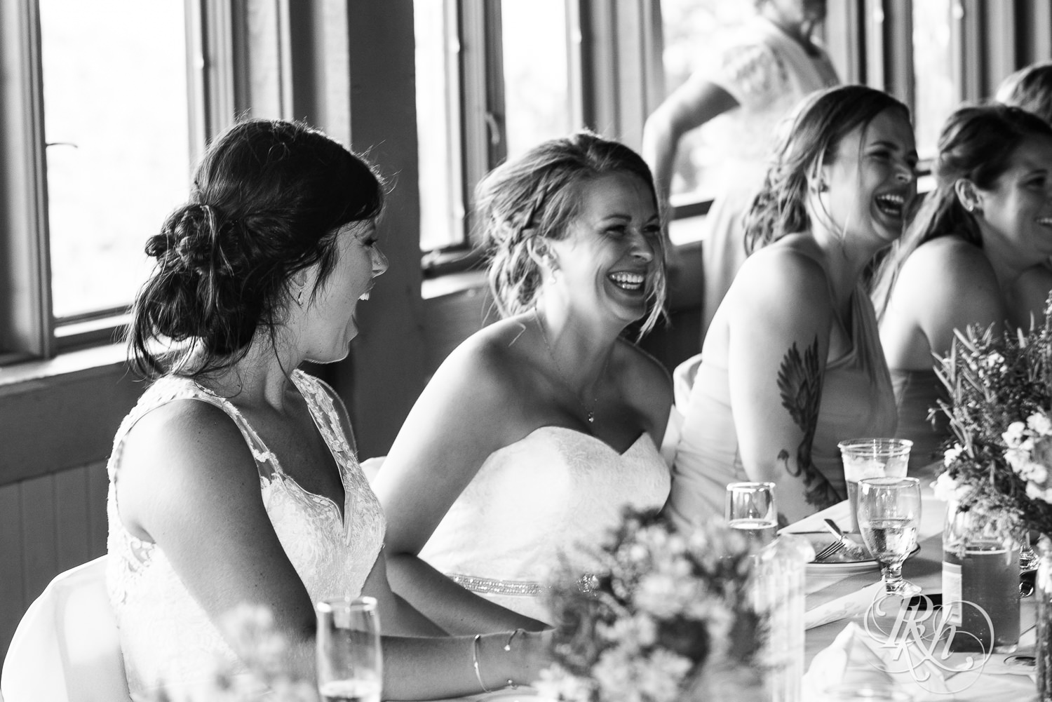Lesbian brides smile at head table during their wedding reception at Spirit Mountain in Duluth, Minnesota.
