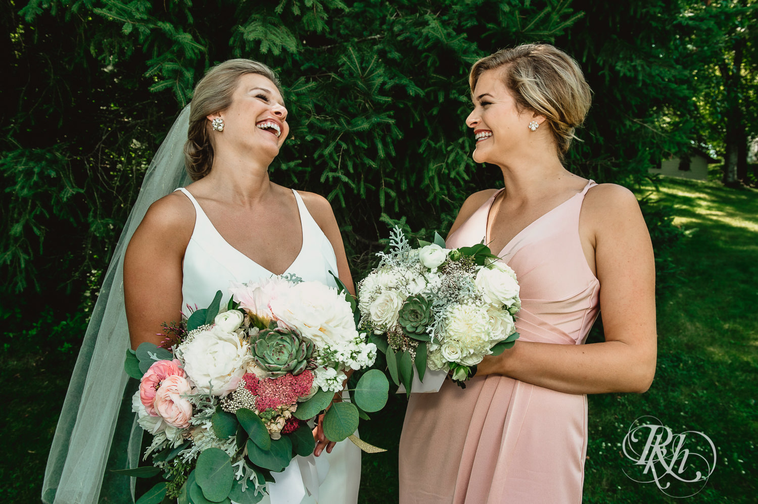 Bride laughs with bridesmaids on her wedding day in the woods in Minneapolis, Minnesota.