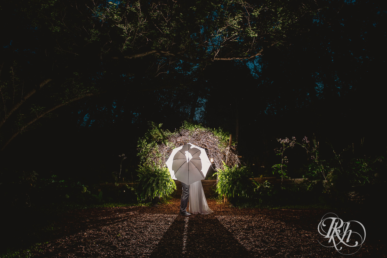 Bride and groom kiss under arch at night at Camrose Hill Flower Farm in Stillwater, Minnesota.