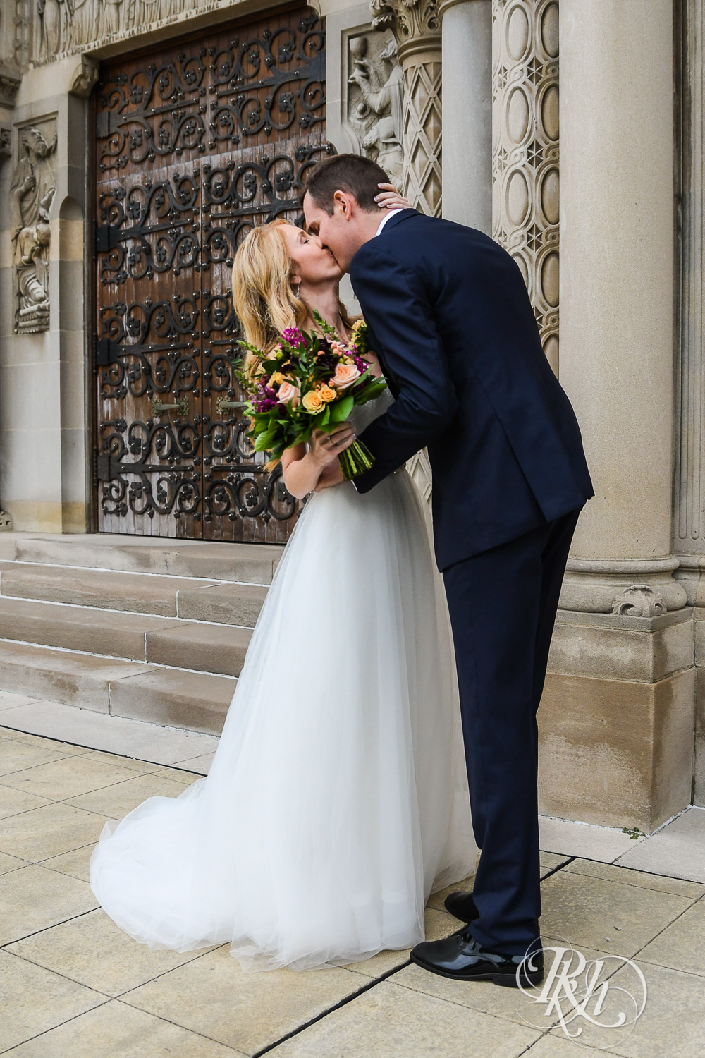 Bride and groom kiss on the steps of St. Thomas Moore Catholic Church in Saint Paul, Minnesota.