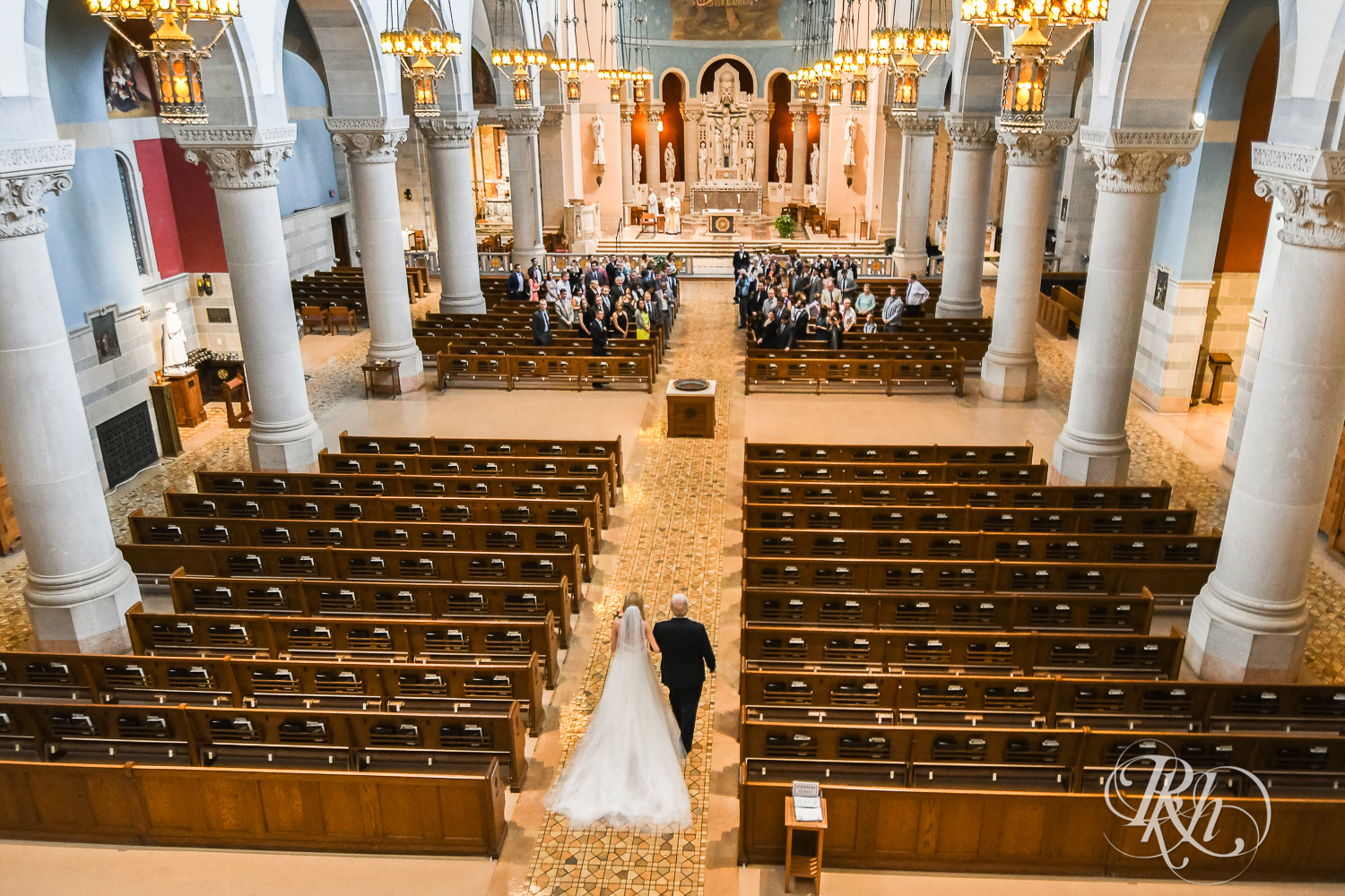 Bride and dad walk down the aisle during wedding ceremony at St. Thomas Moore Catholic Church in Saint Paul, Minnesota.