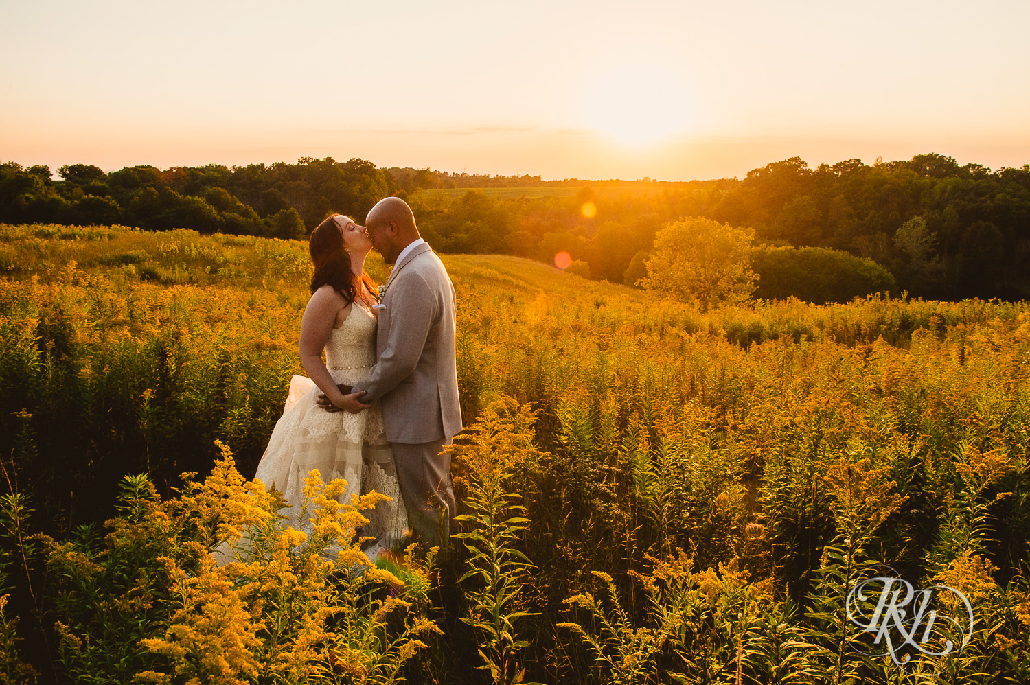 Bride and Asian groom kiss during sunset in field on a hill at Birch Hill Barn in Glenwood City, Wisconsin.