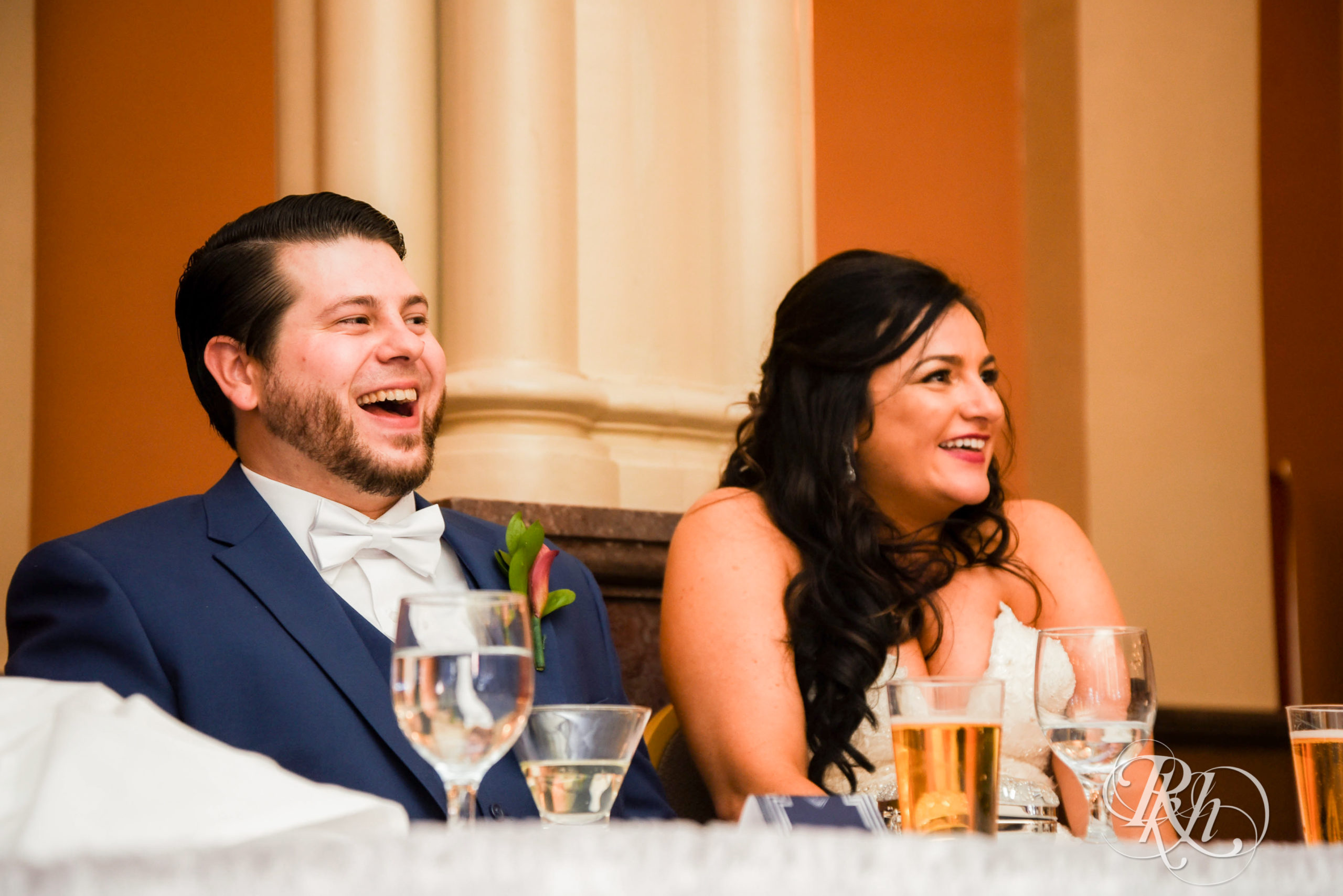 Bride and groom smile during speeches on wedding day at Landmark Center in Saint Paul, Minnesota.