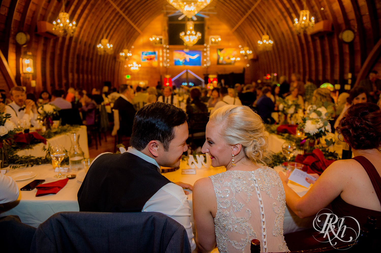 Bride and groom smile at head table at Green Acres Event Center barn wedding in Eden Prairie, Minnesota.