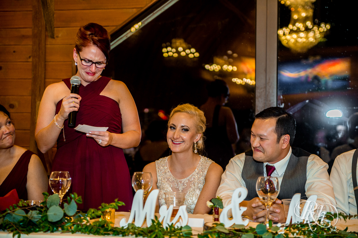 Bride and groom smile at head table at Green Acres Event Center barn wedding in Eden Prairie, Minnesota.