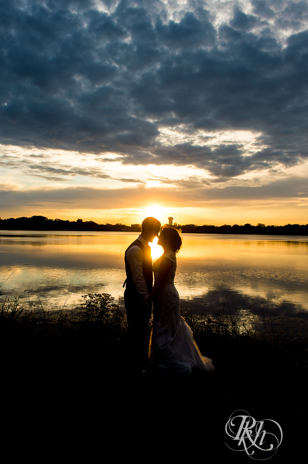 Bride and groom kiss at sunset in front of the lake in White Bear Lake, Minnesota.