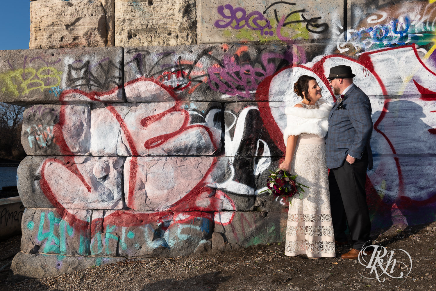 Bride and groom smile in front of graffiti wall in Minneapolis, Minnesota.