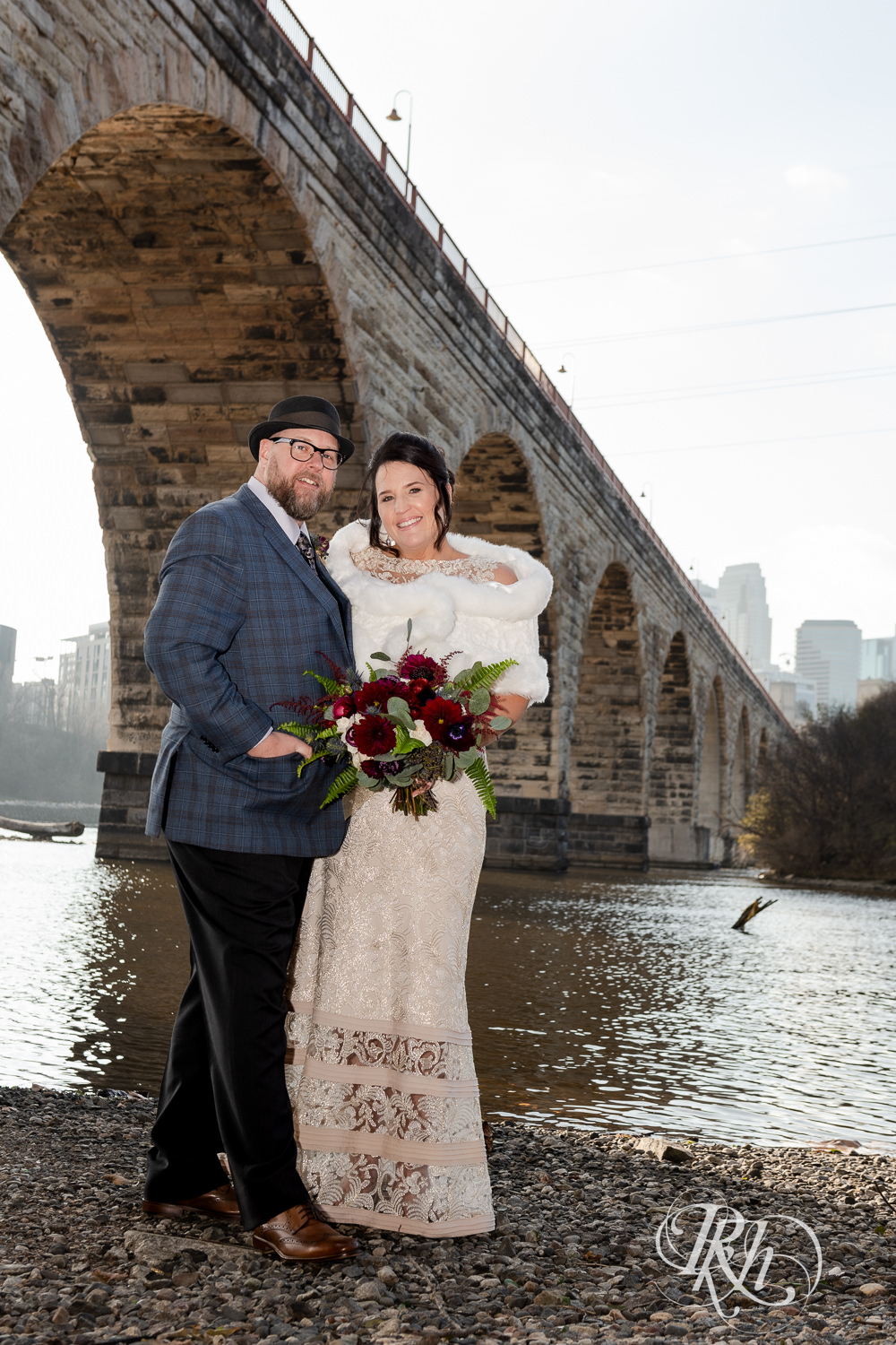 Bride and groom smile under Stone Arch Bridge in Minneapolis, Minnesota.