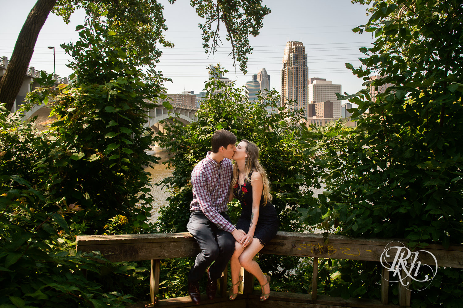 Man and woman in black lace dress kiss in Saint Anthony Main in Minneapolis, Minnesota in front of the city skyline.