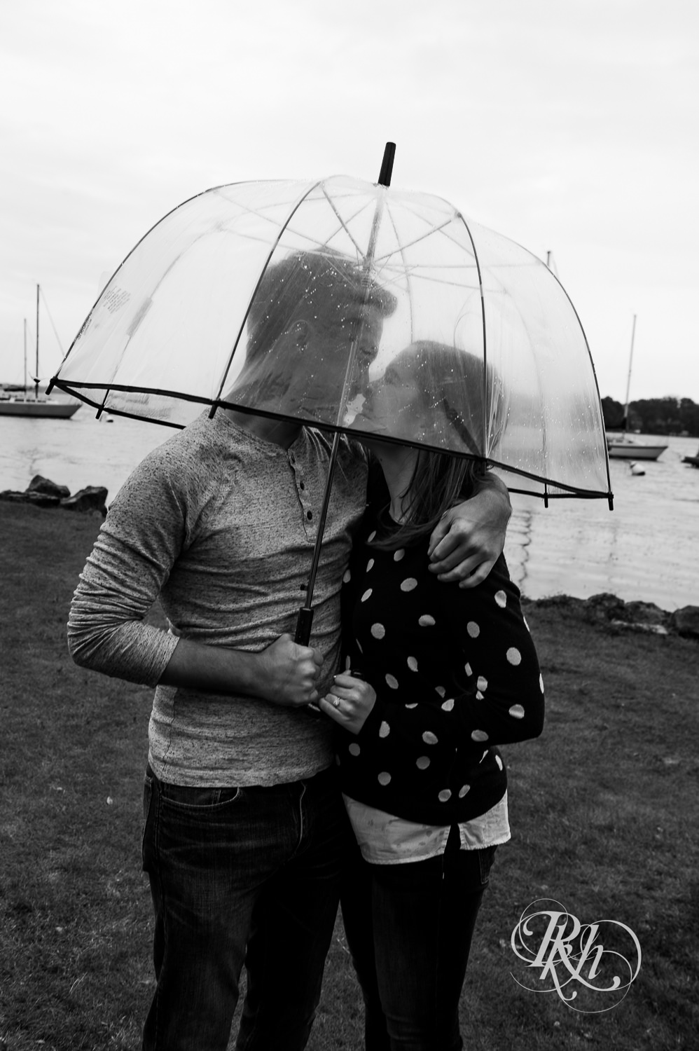 Man and woman laugh under umbrella during rainy day engagement photos in Excelsior, Minnesota.