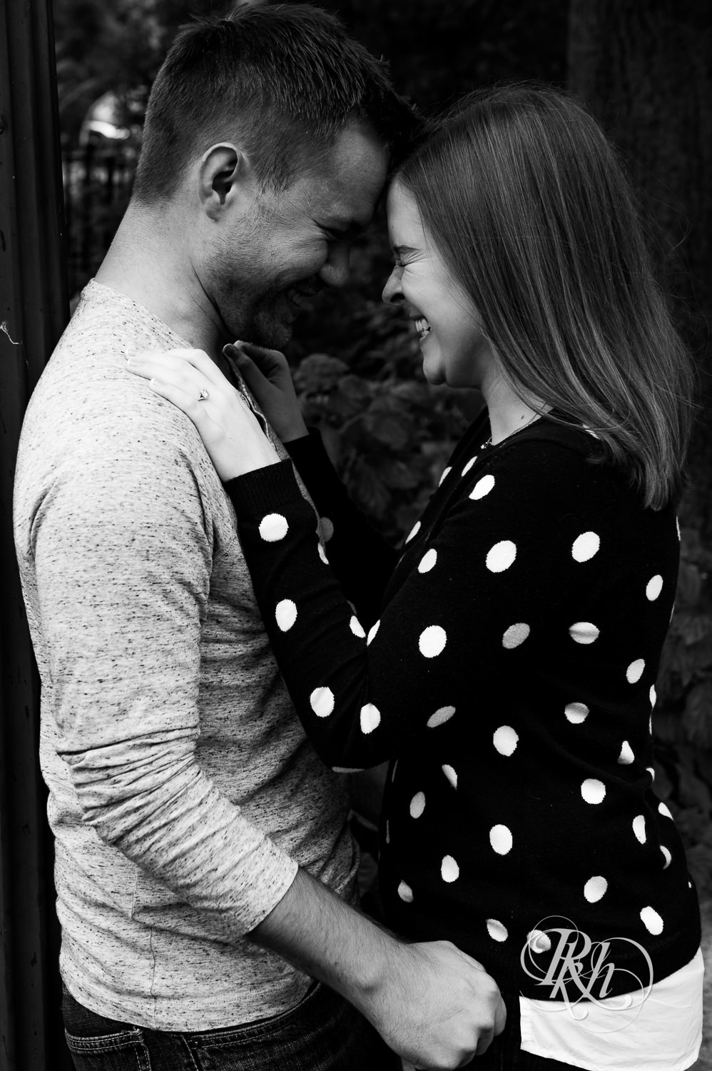 Man and woman in sweaters and jeans laugh during rainy day engagement photos in Excelsior, Minnesota.
