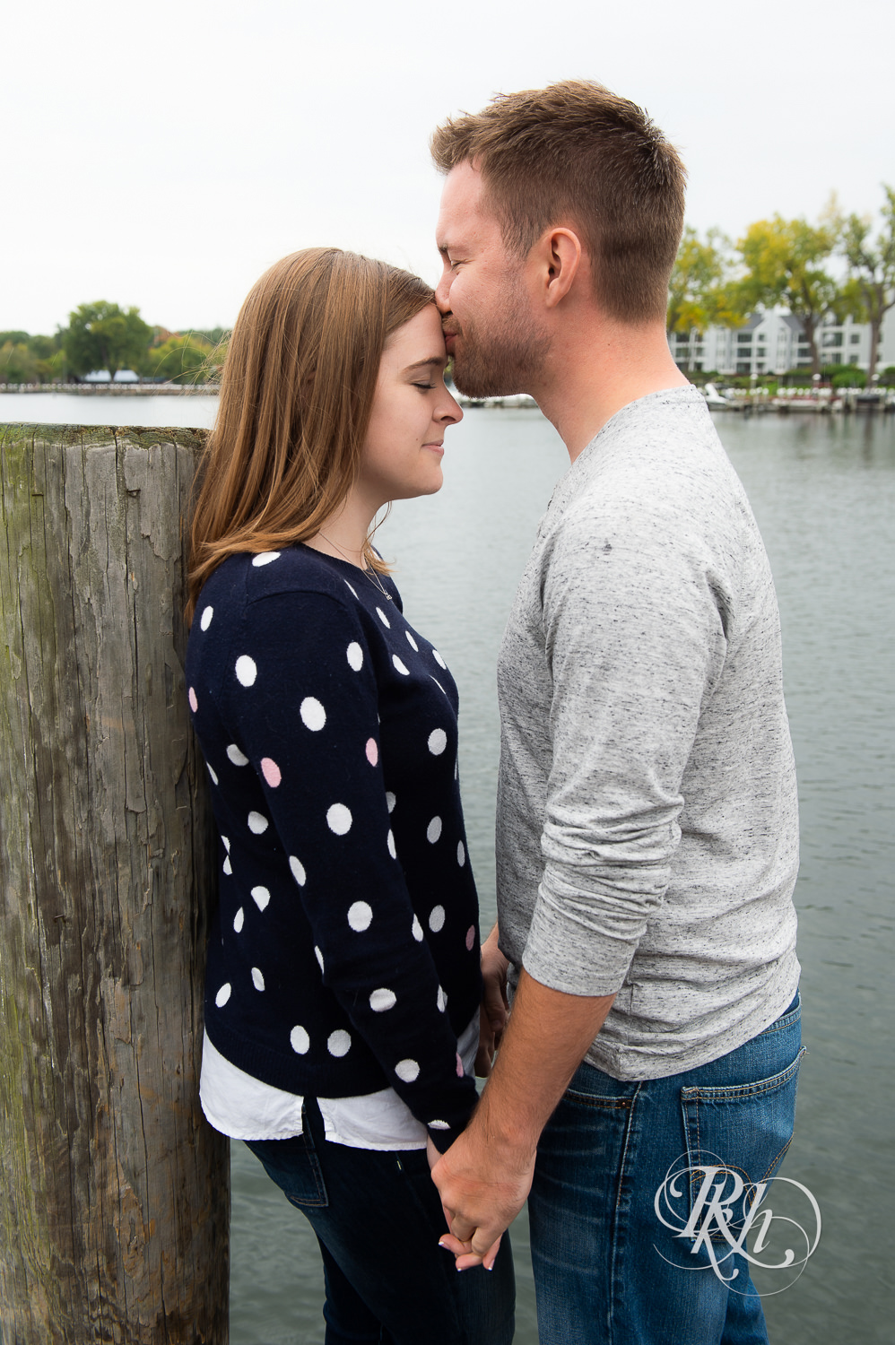 Man and woman in sweaters and jeans kiss during rainy day engagement photos in Excelsior, Minnesota.