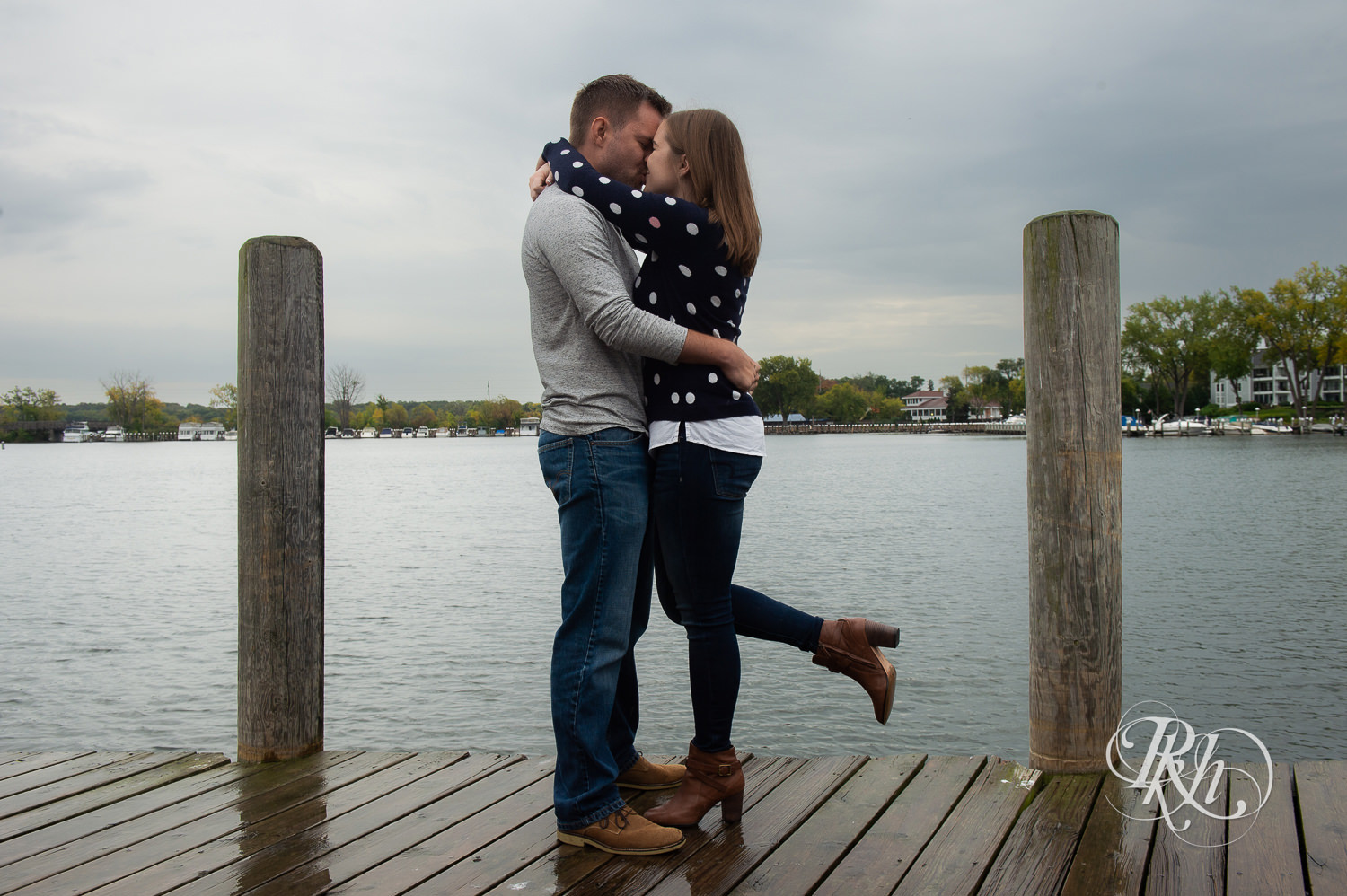 Man and woman in sweaters and jeans kiss during rainy day engagement photos in Excelsior, Minnesota.