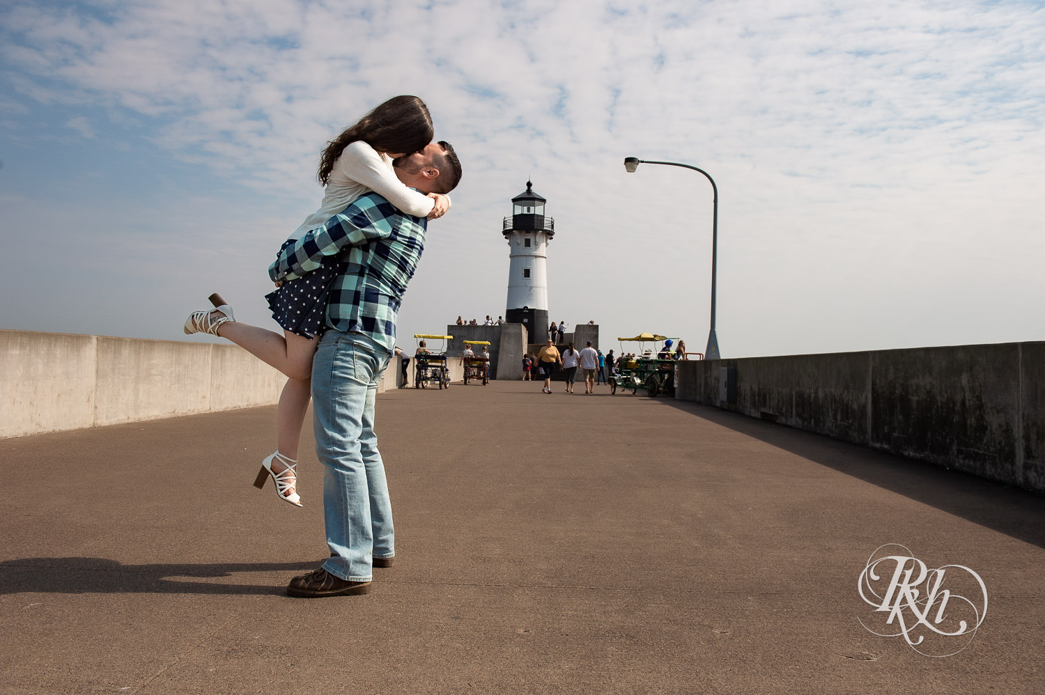 Man and woman kiss with lighthouse in background during Canal Park engagement photos in Duluth, Minnesota.