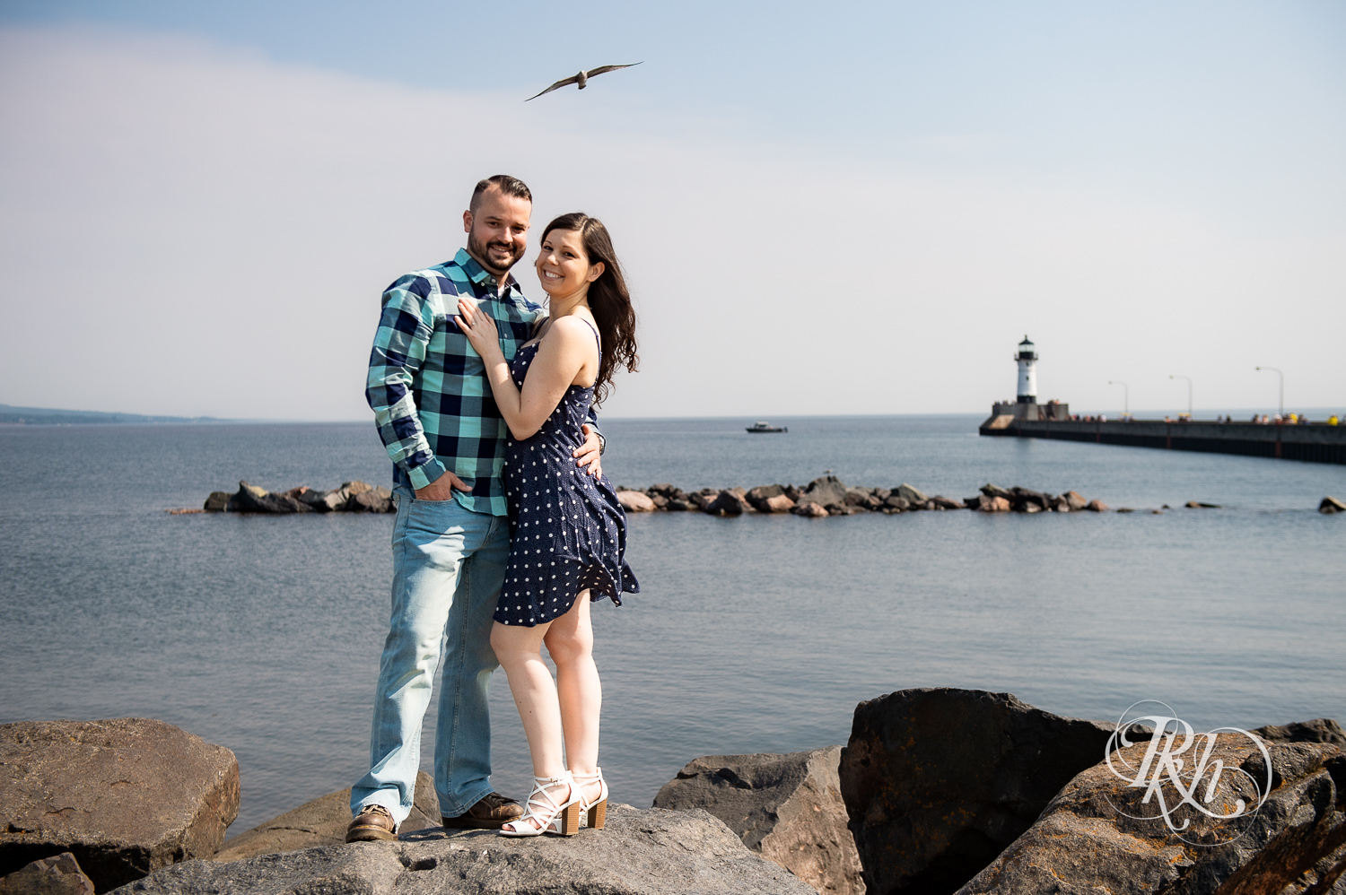 Man and woman smile in front of Lake Superior in Canal Park in Duluth, Minnesota with bird flying over them.