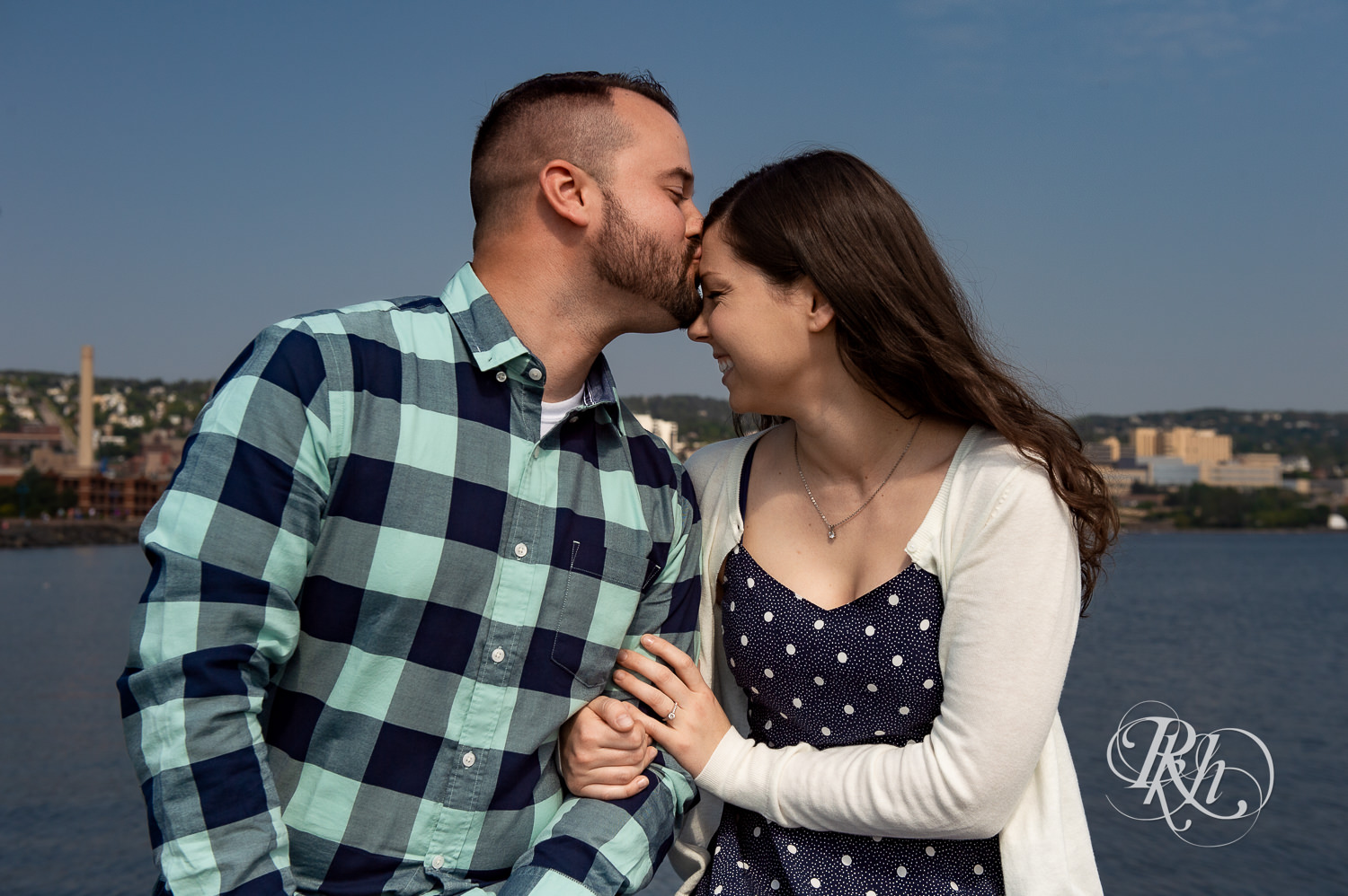 Man and woman kiss with city in background during Canal Park engagement photos in Duluth, Minnesota.