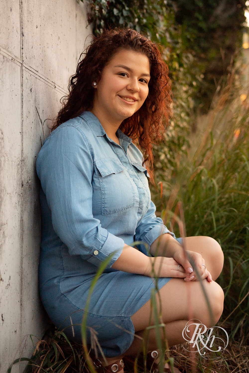 Senior girl in denim dress with curly hair smiles during sunset in Minneapolis, Minnesota.