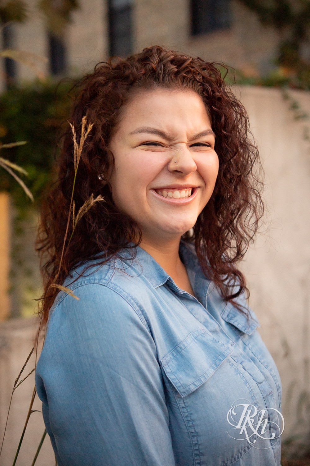 Senior girl in denim dress with curly hair smiles during sunset in Minneapolis, Minnesota.