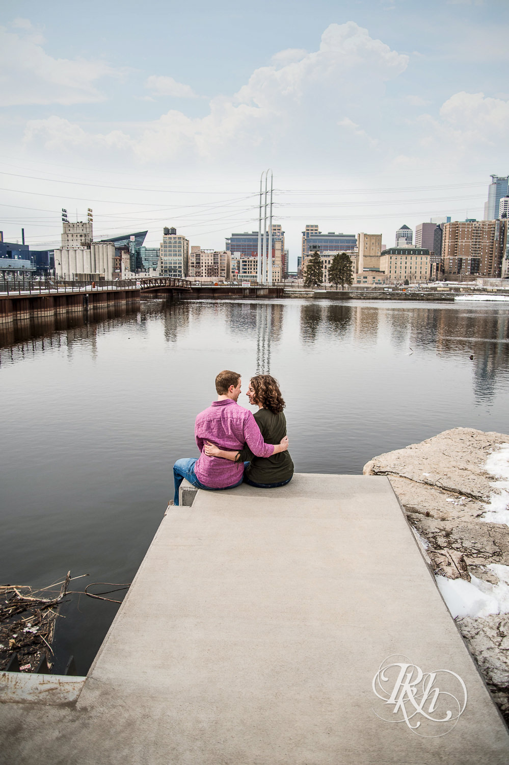 Man and woman smile in front of the river and Minneapolis skyline.