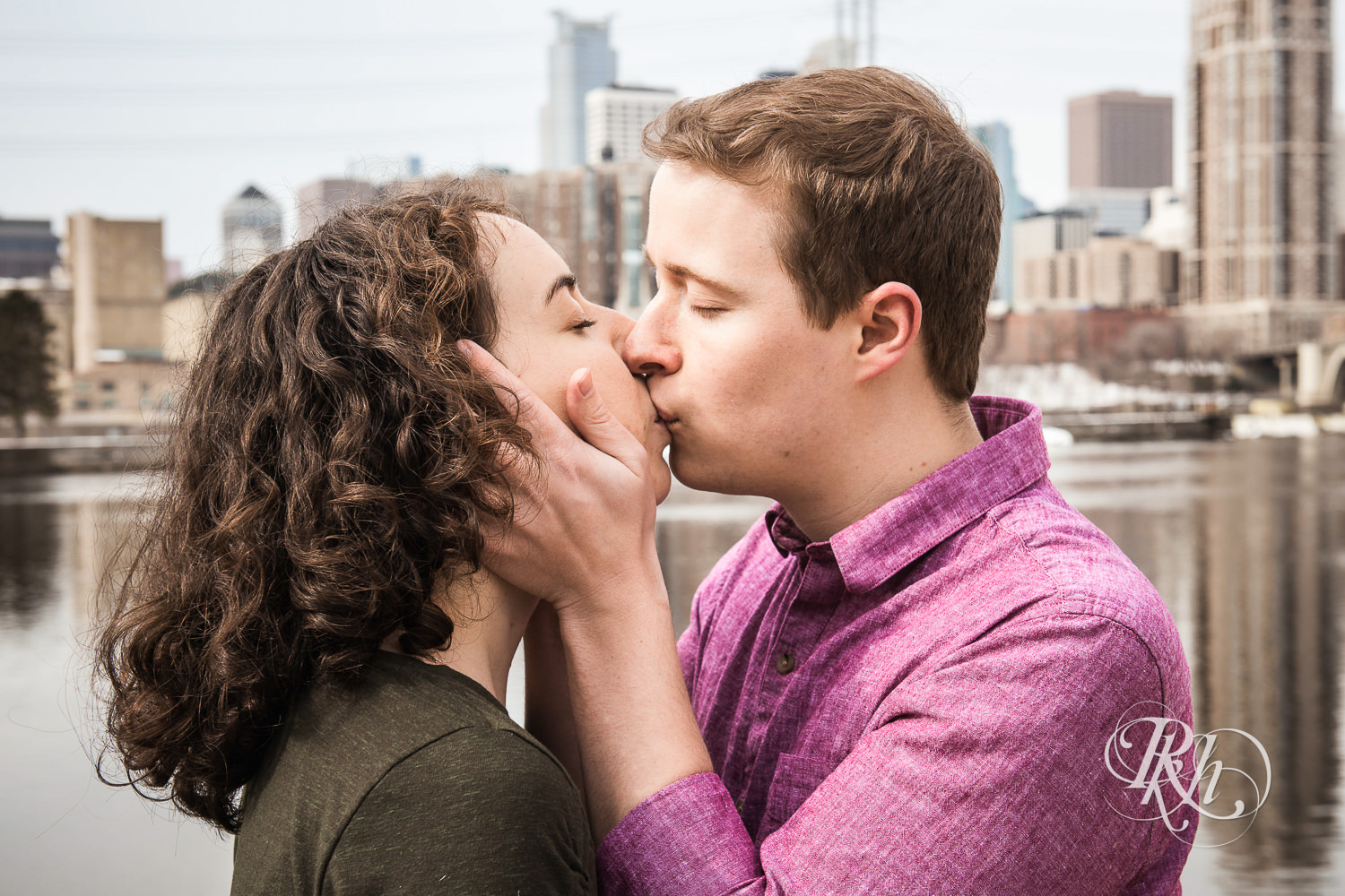 Man and woman kiss in front of the river and Minneapolis skyline.