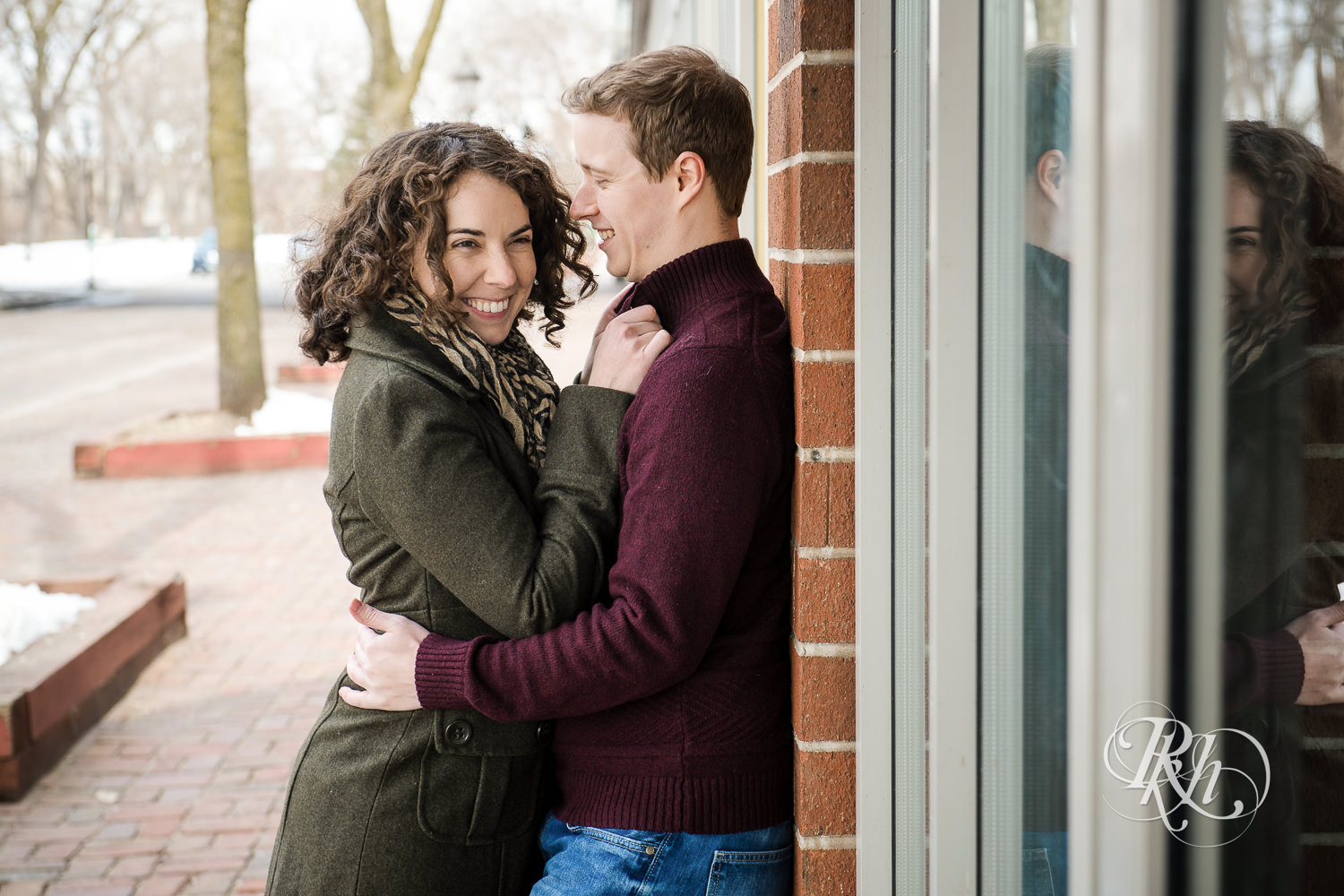 Man and woman smile during winter St. Anthony Main engagement photos in Minneapolis, Minnesota.