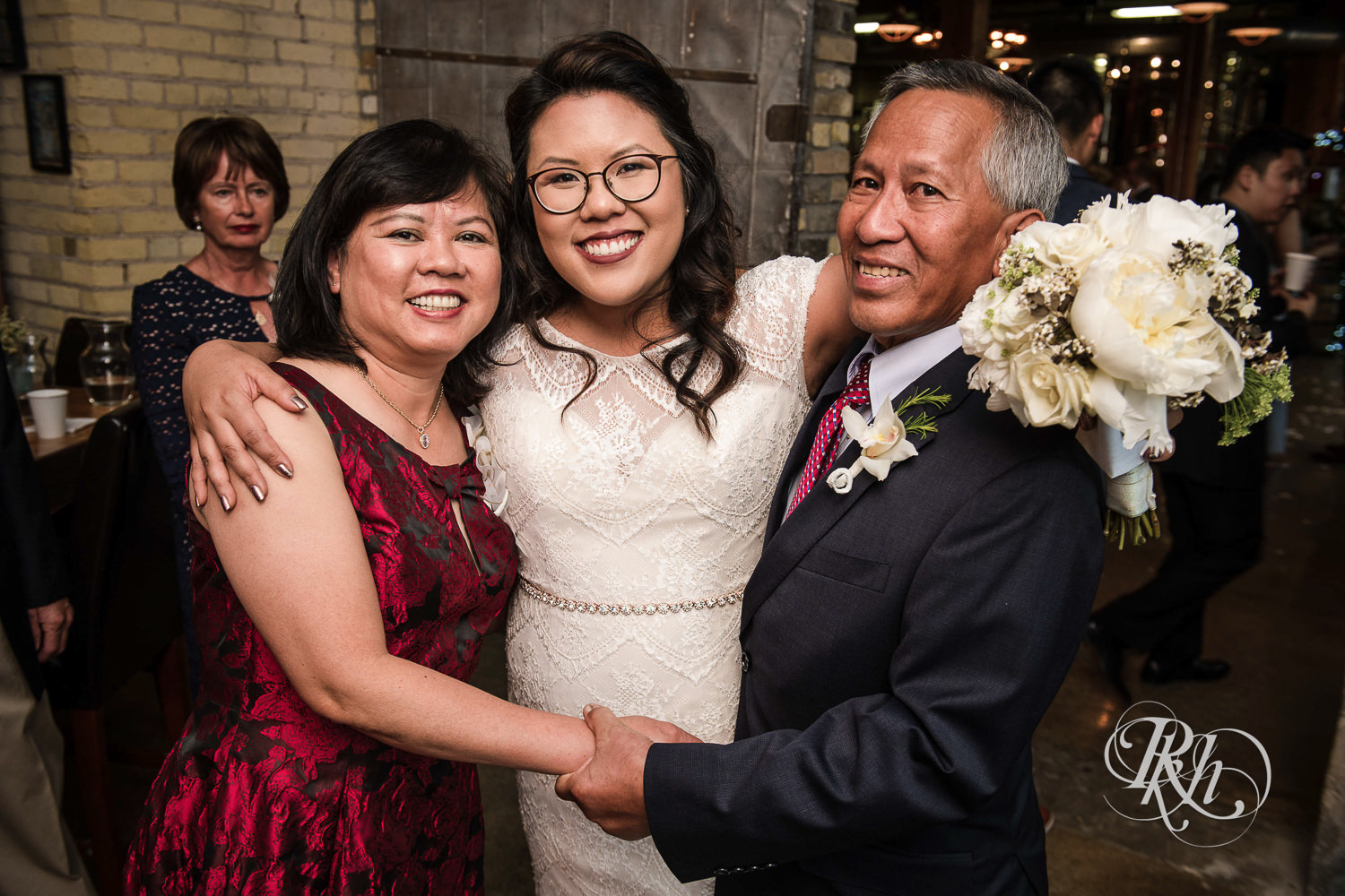 Asian bride with glasses smiles with parents at 612 Brew in Minneapolis, Minnesota.