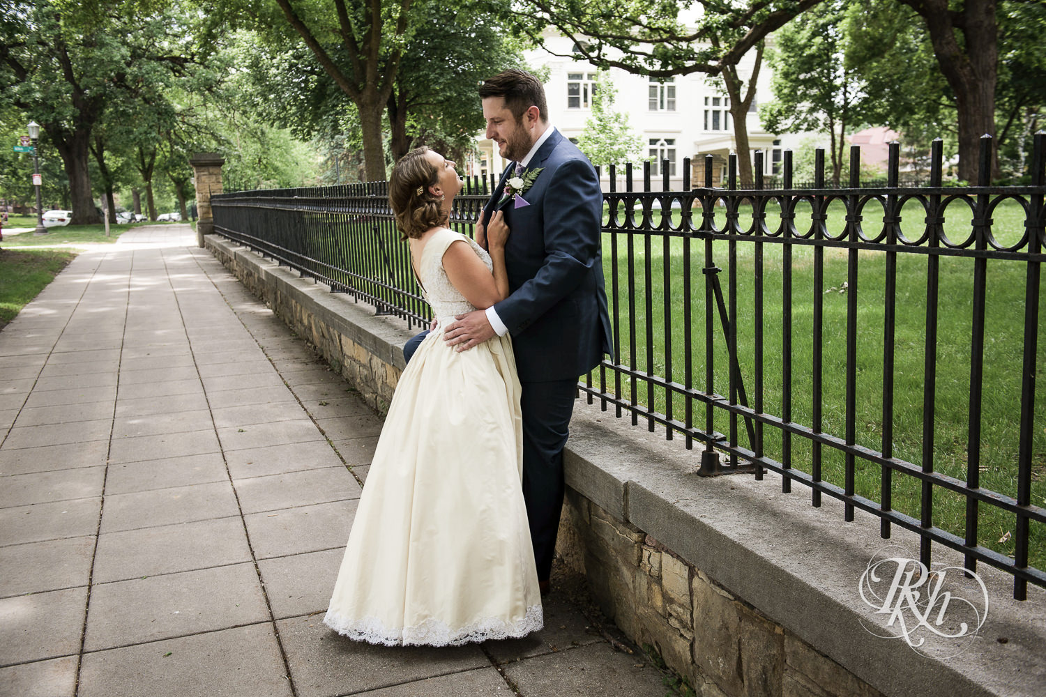 Bride and groom smile against fence at Summit Manor Reception House in Saint Paul, Minnesota.