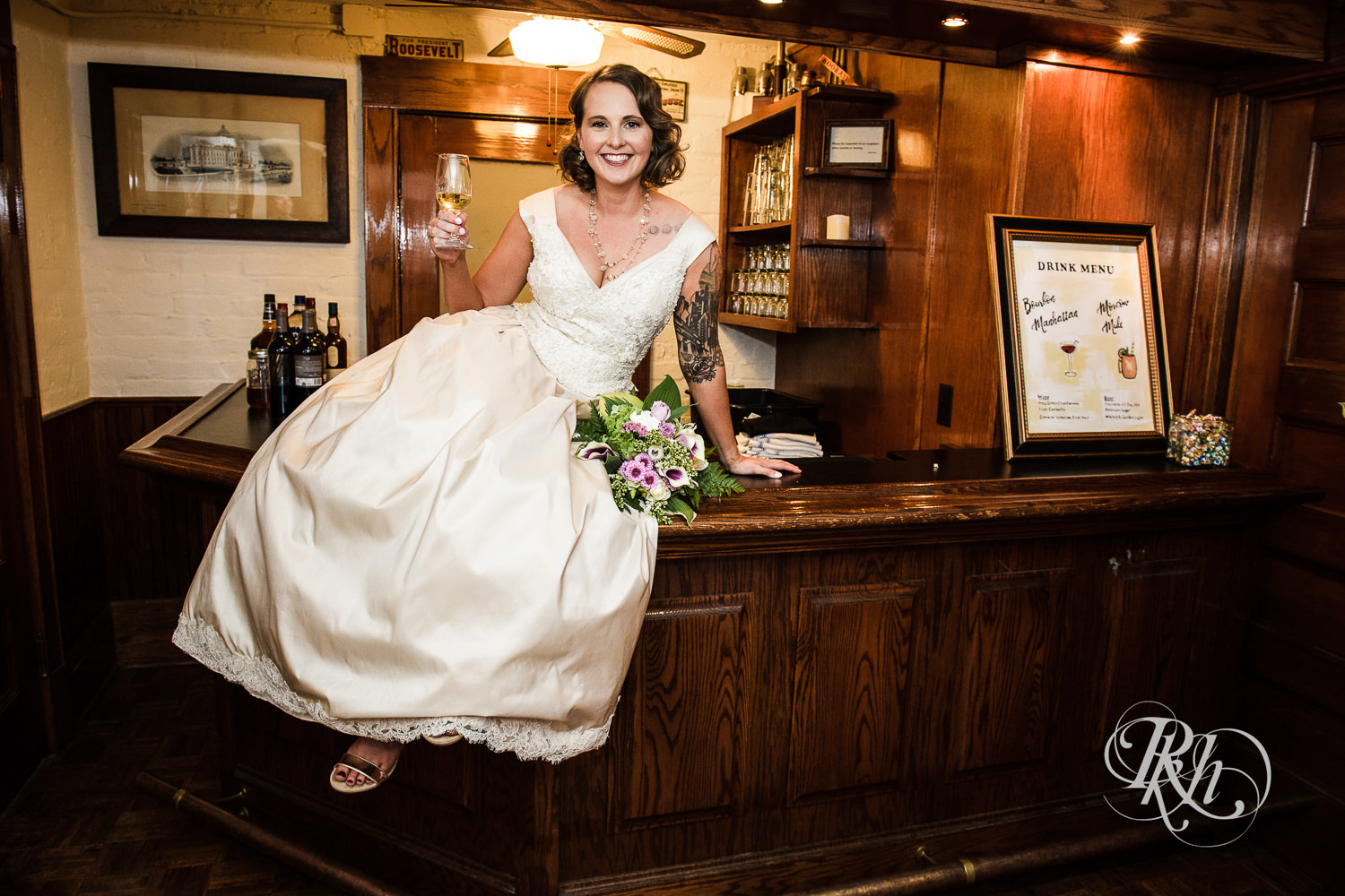 Bride sits on the bar with a drink at Summit Manor Reception House in Saint Paul, Minnesota.