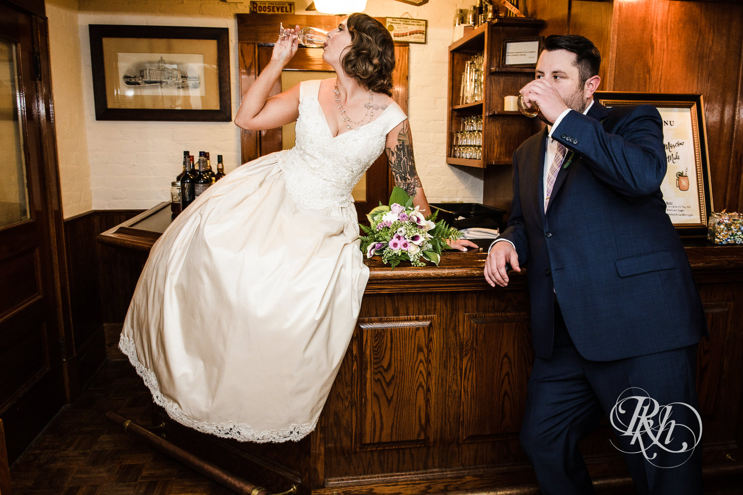 Bride sits on the bar with a drink next to the groom at Summit Manor Reception House in Saint Paul, Minnesota.