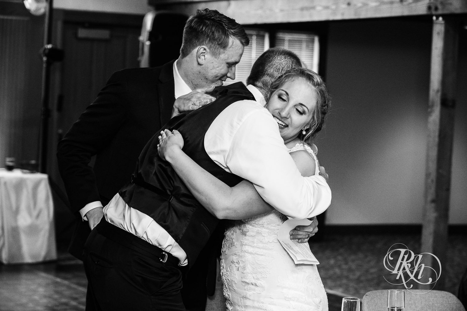 Bride hugs groomsmen during speeches at wedding reception at Earle Brown Heritage Center in Brooklyn Center, Minnesota.