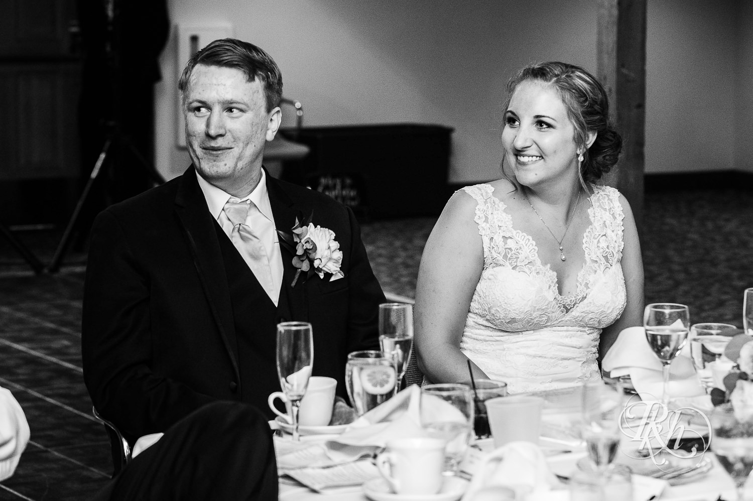 Bride and groom smile during speeches at wedding reception at Earle Brown Heritage Center in Brooklyn Center, Minnesota.