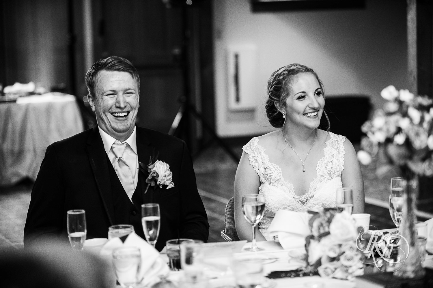 Bride and groom smile during speeches at wedding reception at Earle Brown Heritage Center in Brooklyn Center, Minnesota.