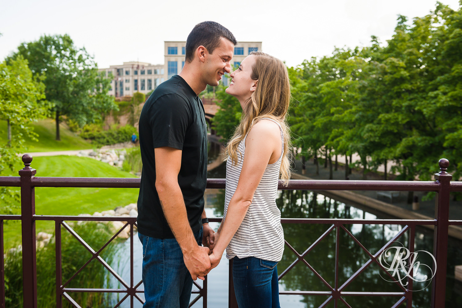 Man and woman in T-shirts and jeans smile on bridge in Centennial Lakes Park in Edina, Minnesota.