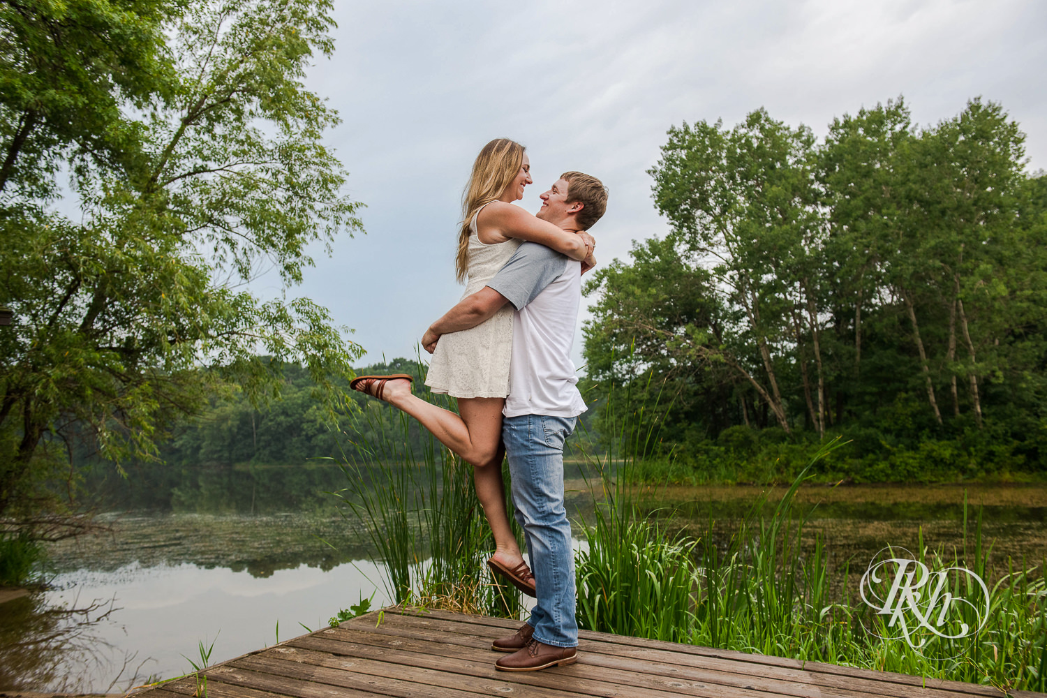 Man in jeans lifts woman in white dress on dock in Lebanon Hills Regional Park in Eagan, Minnesota.