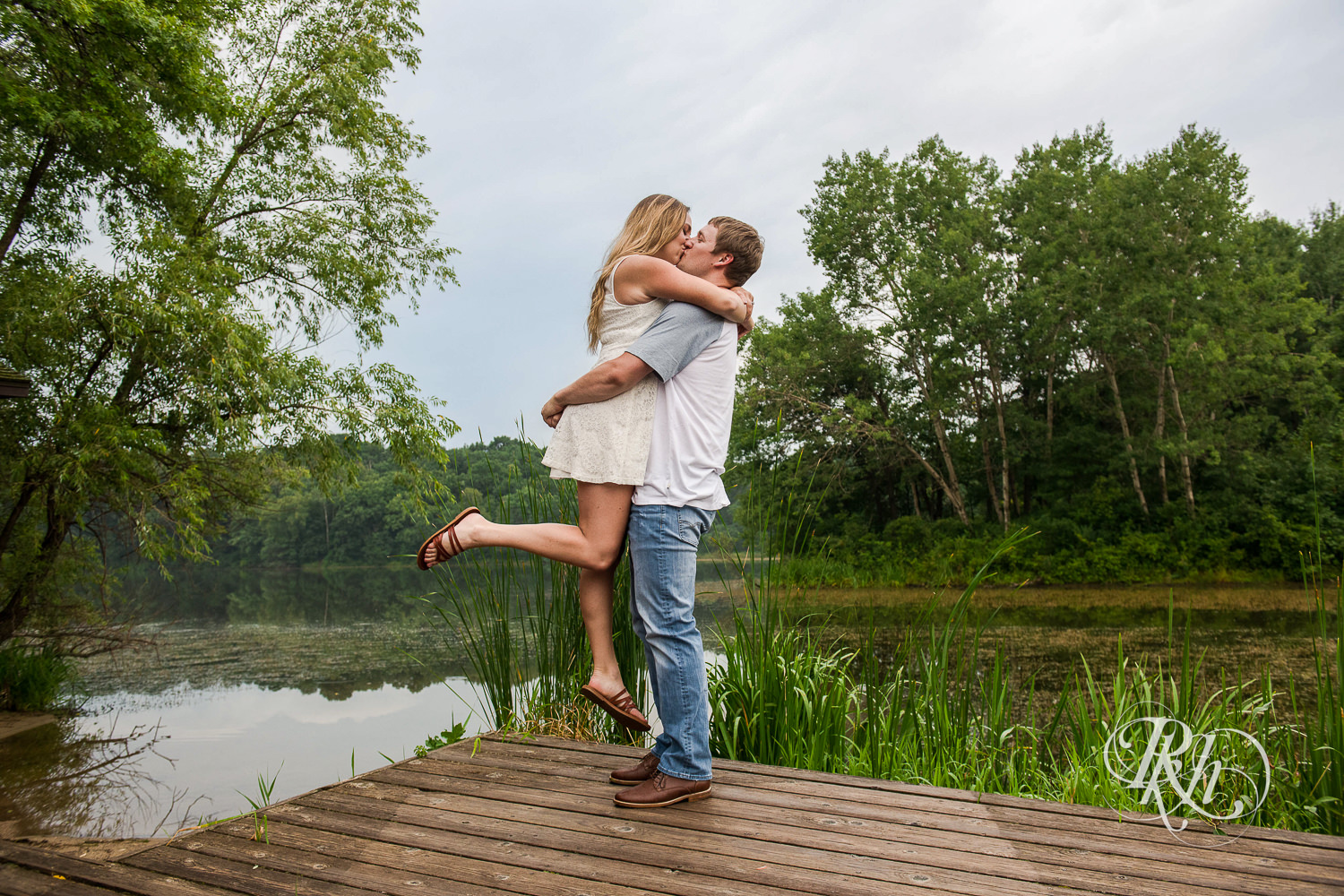 Man in jeans kisses woman in white dress on dock in Lebanon Hills Regional Park in Eagan, Minnesota.