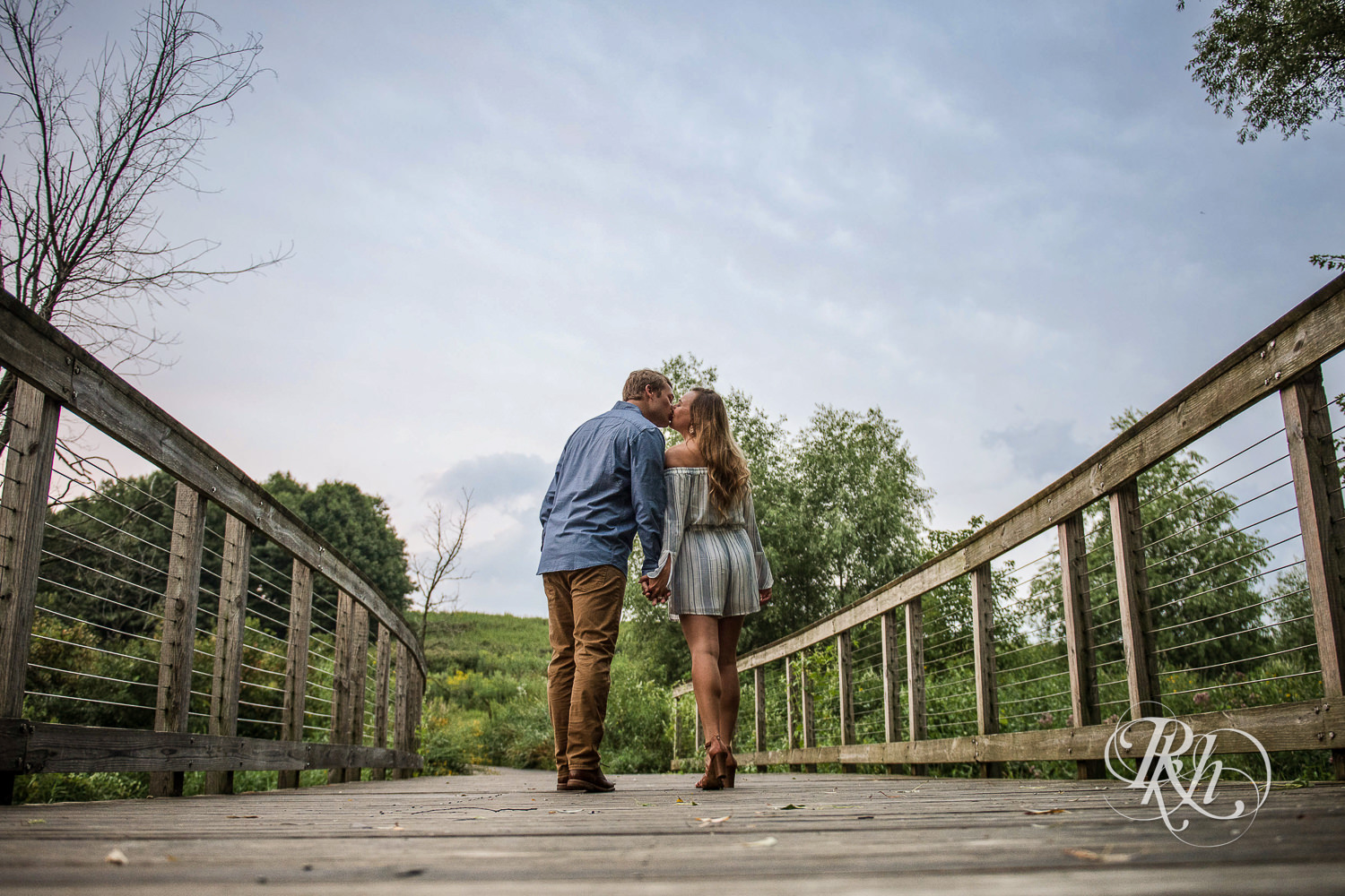 Man and woman kiss on bridge at sunrise in Lebanon Hills Regional Park in Eagan, Minnesota.