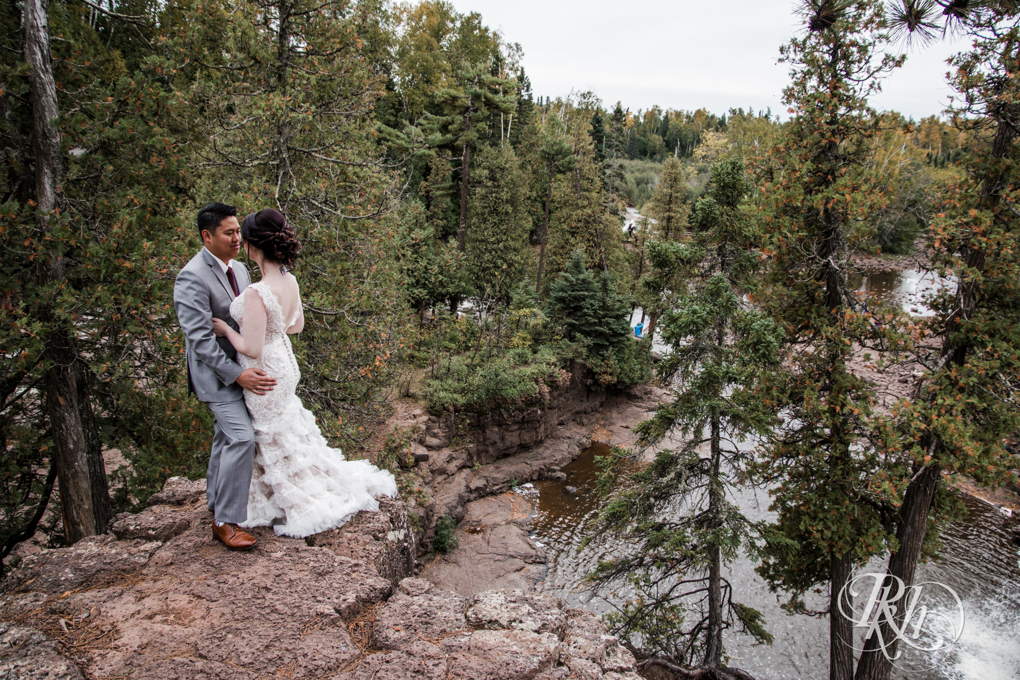 Bride and groom smile on cliff at Gooseberry Falls in Two Harbors, Minnesota.