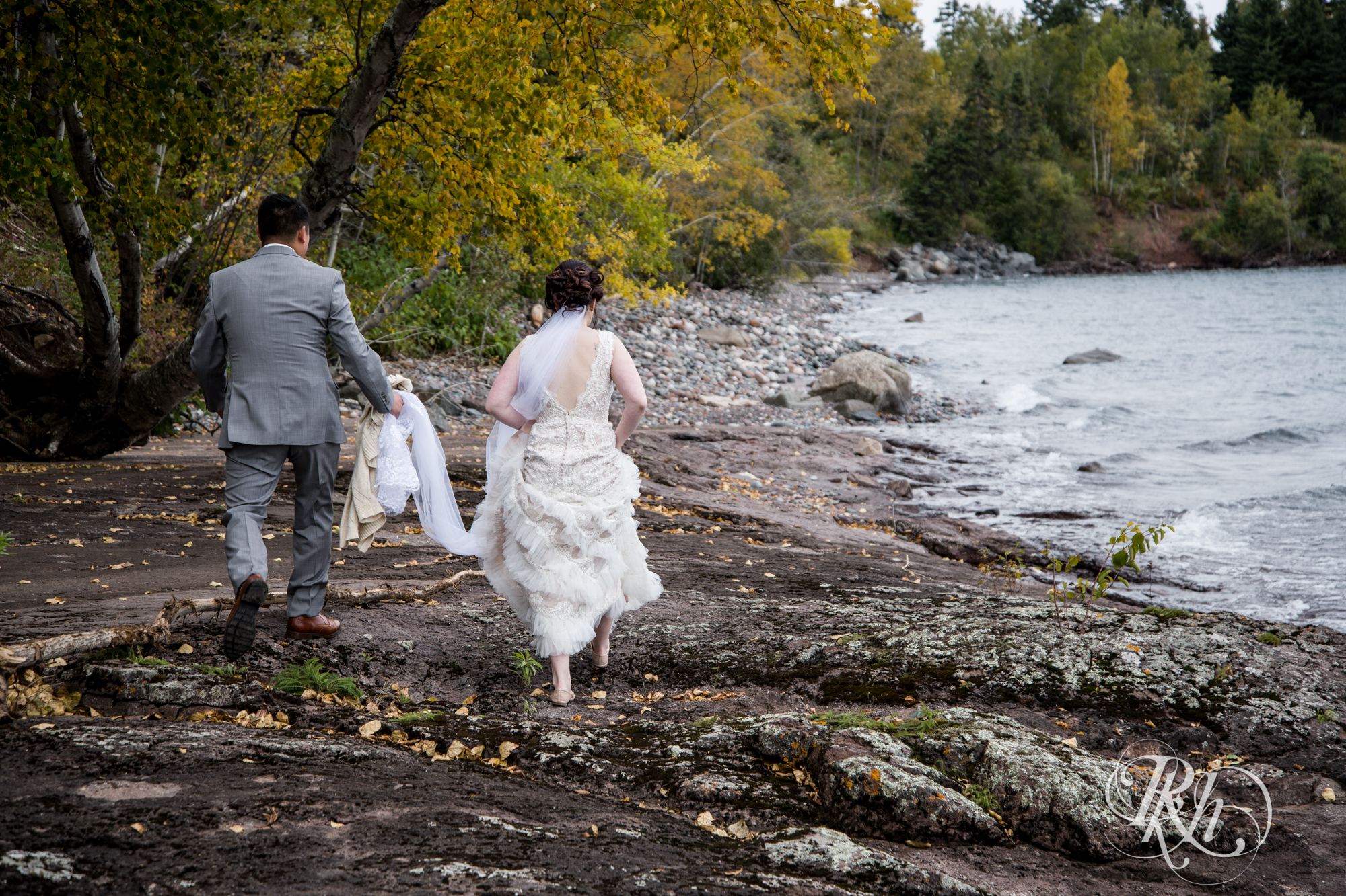 Bride and groom walk on beach in front of Lake Superior at Grand Superior Lodge in Two Harbors, Minnesota.