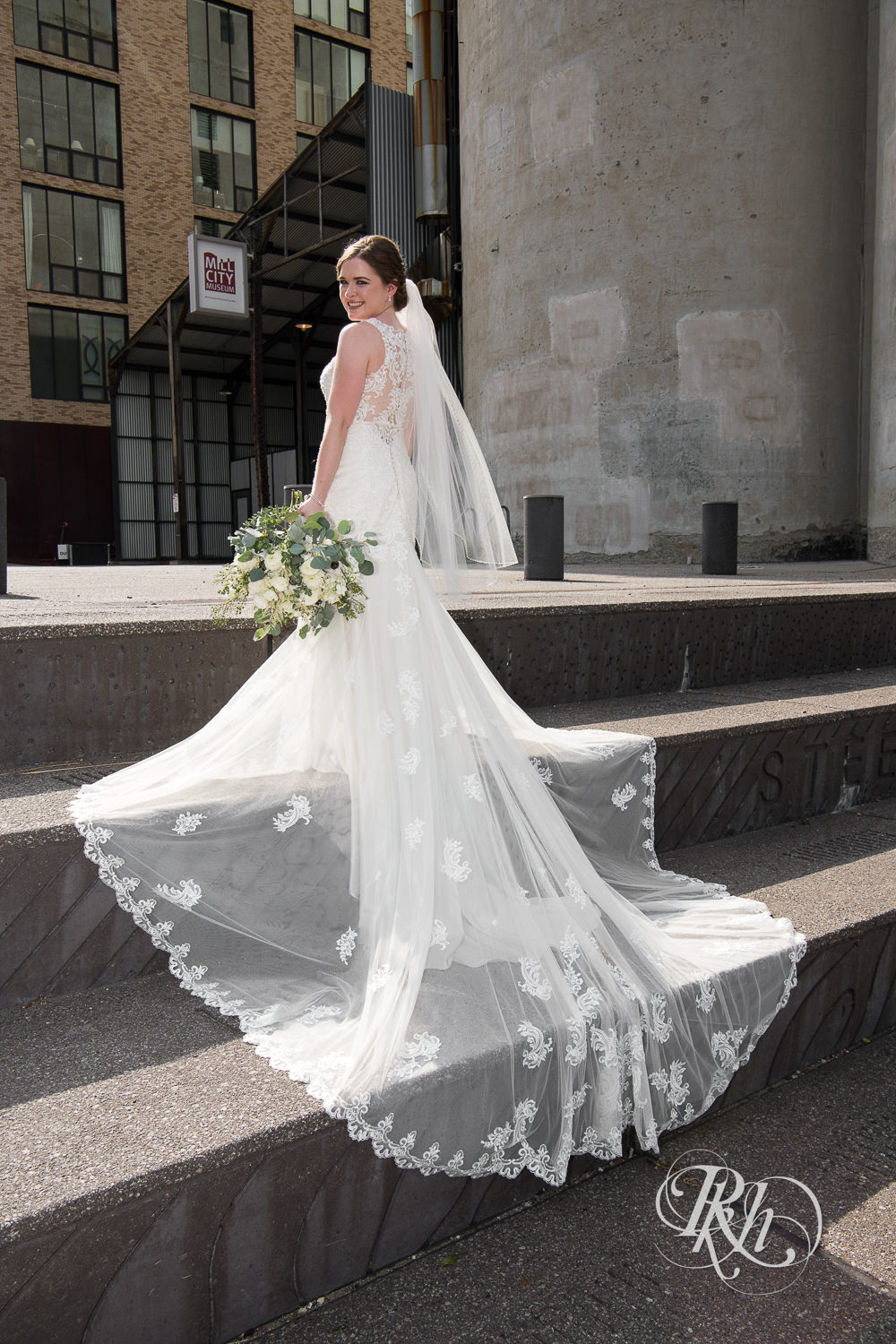 Bride with long veil holds flowers and stands on stairs in Minneapolis, Minnesota.
