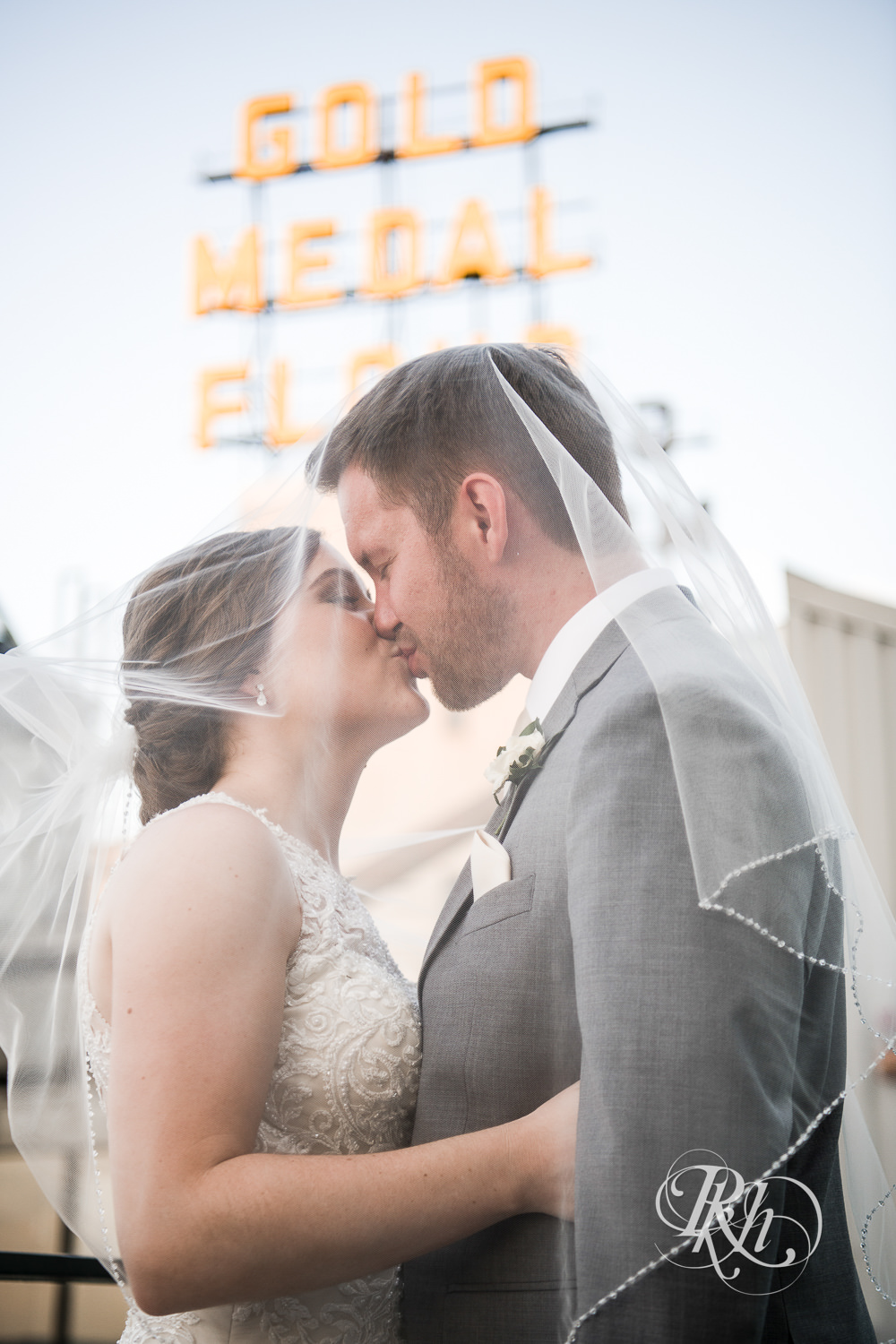 Bride and groom kiss under veil in front of the Gold Medal Flour sign in Minneapolis, Minnesota.