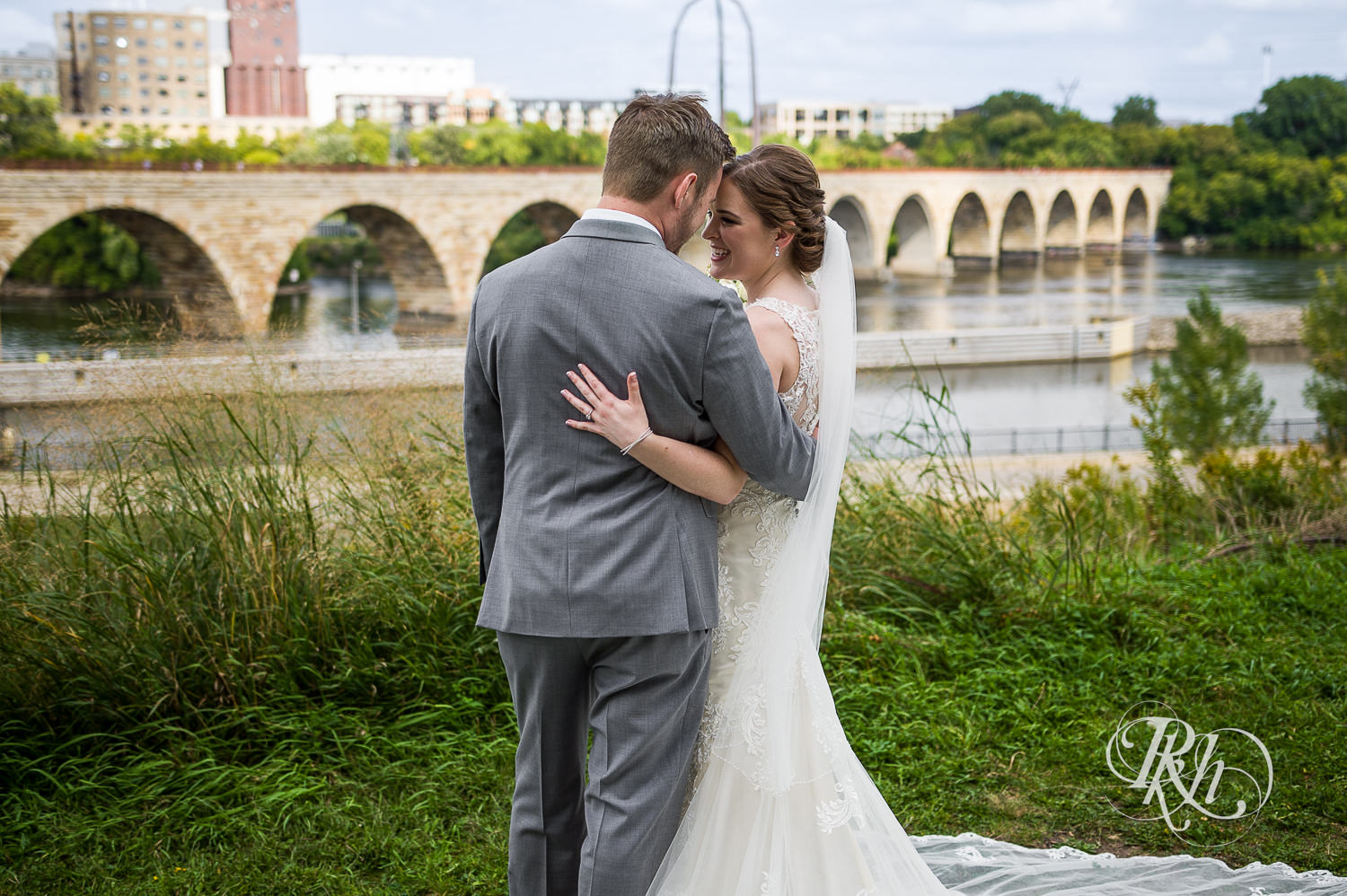 Bride and groom smile in front of Minneapolis skyline at Mill City Museum in Minneapolis, Minnesota.