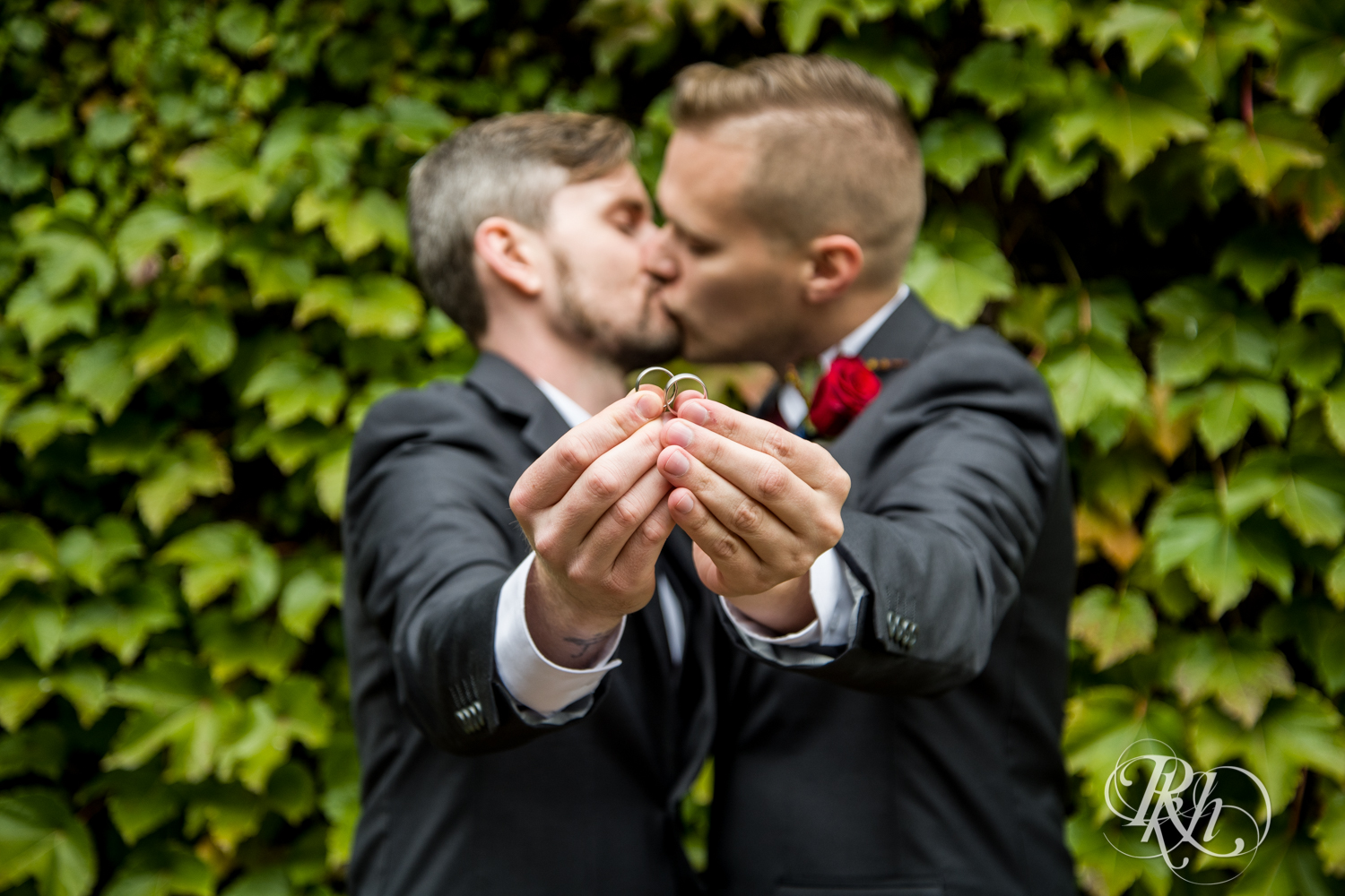 Grooms kiss holding rings in Minneapolis, Minnesota for Minnesota LGBT wedding photographer.