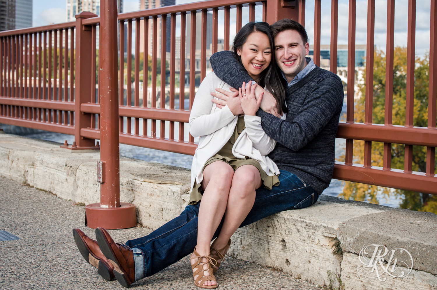 Man in sweater and Asian woman smile on Stone Arch Bridge in Minneapolis, Minnesota.