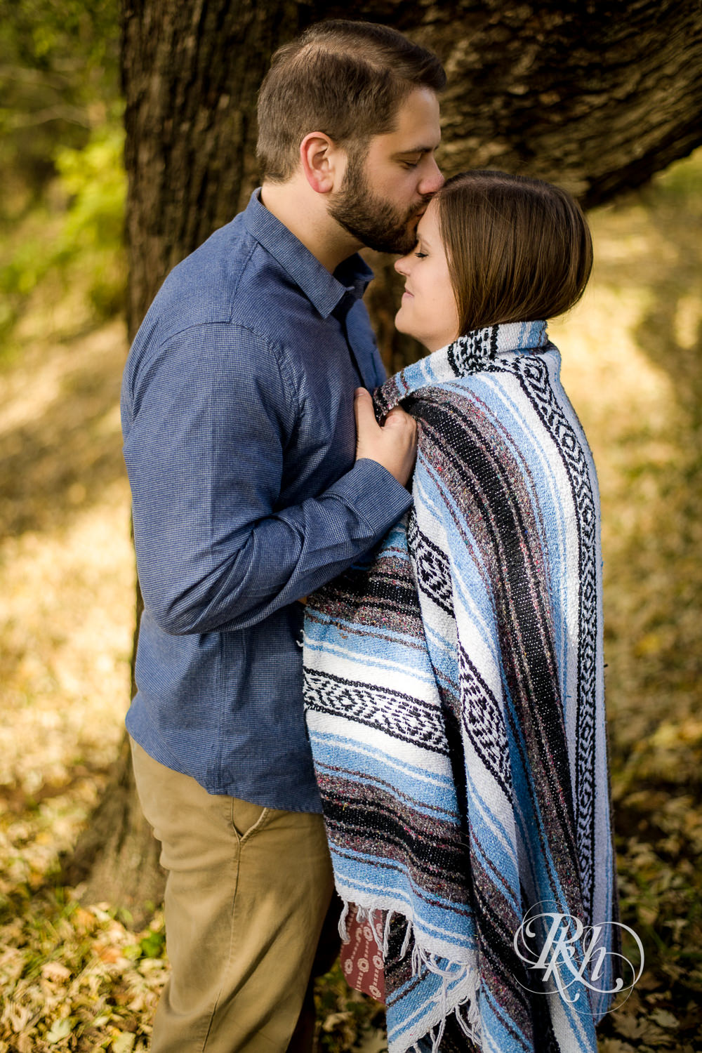 Man and woman kiss in leaves during engagement photography session at home in Annandale, Minnesota.