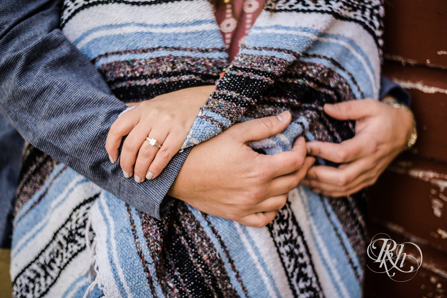 Man and woman snuggle in blanket showing engagement ring.