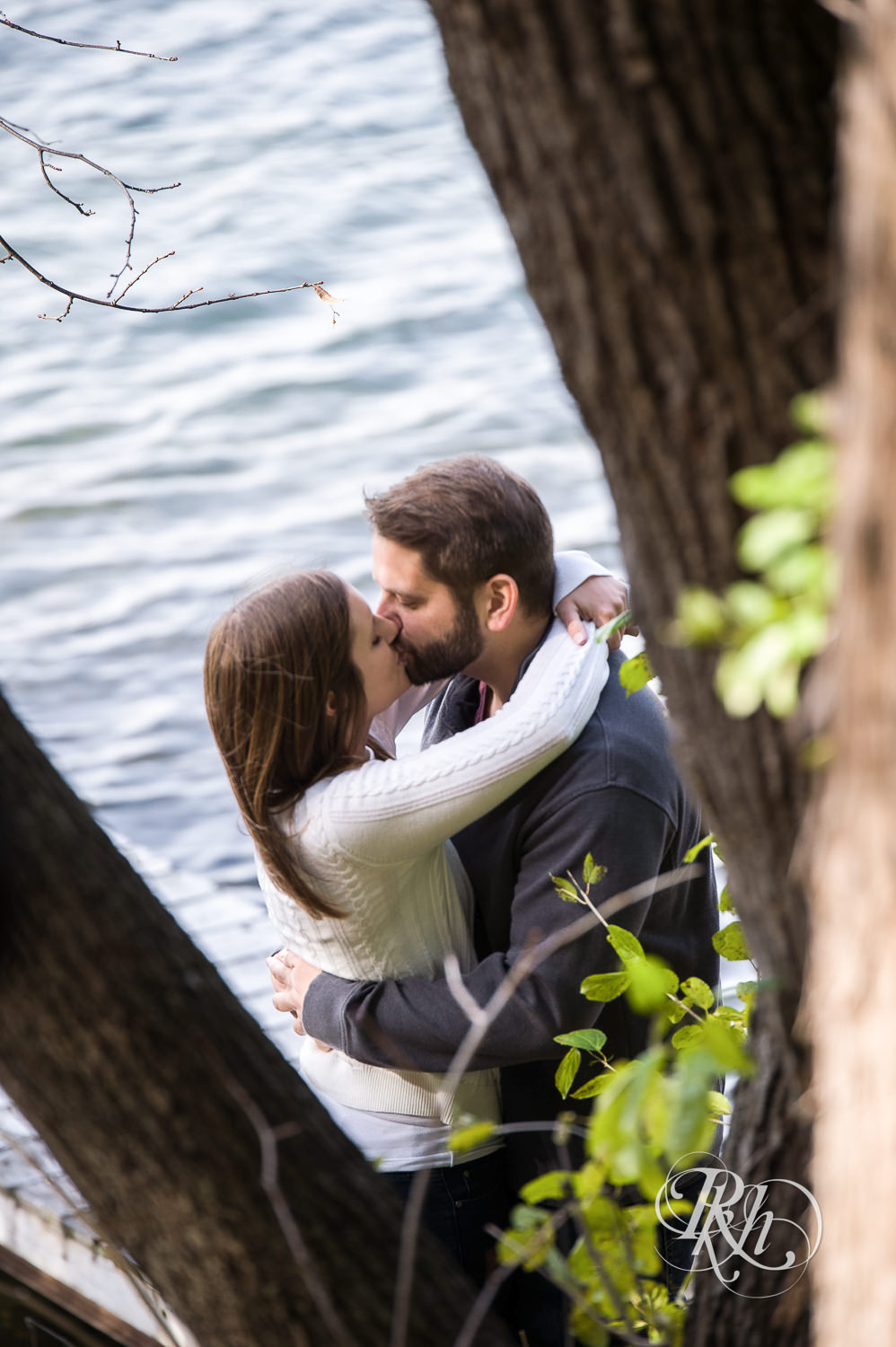 Man and woman kiss in front of lake during engagement photography session at home in Annandale, Minnesota.
