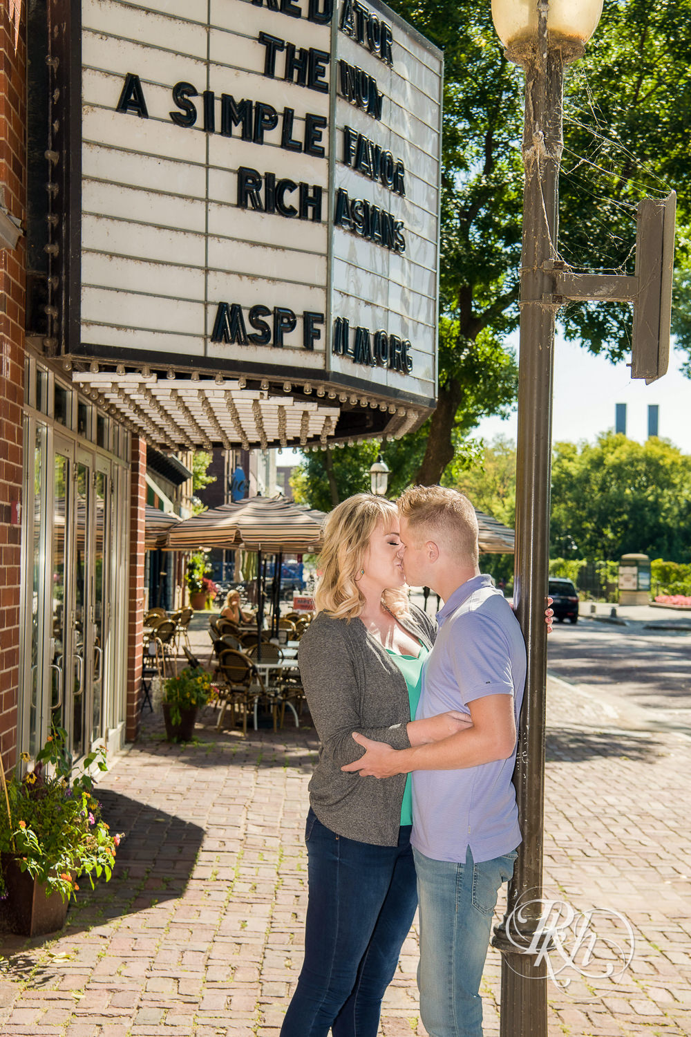 Man and woman kiss in front of a theater during Minneapolis summer engagement photos in Saint Anthony Main. 