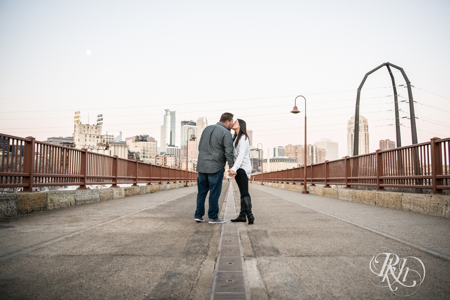 Man and woman kiss on the Stone Arch Bridge in Minneapolis, Minnesota at sunrise.